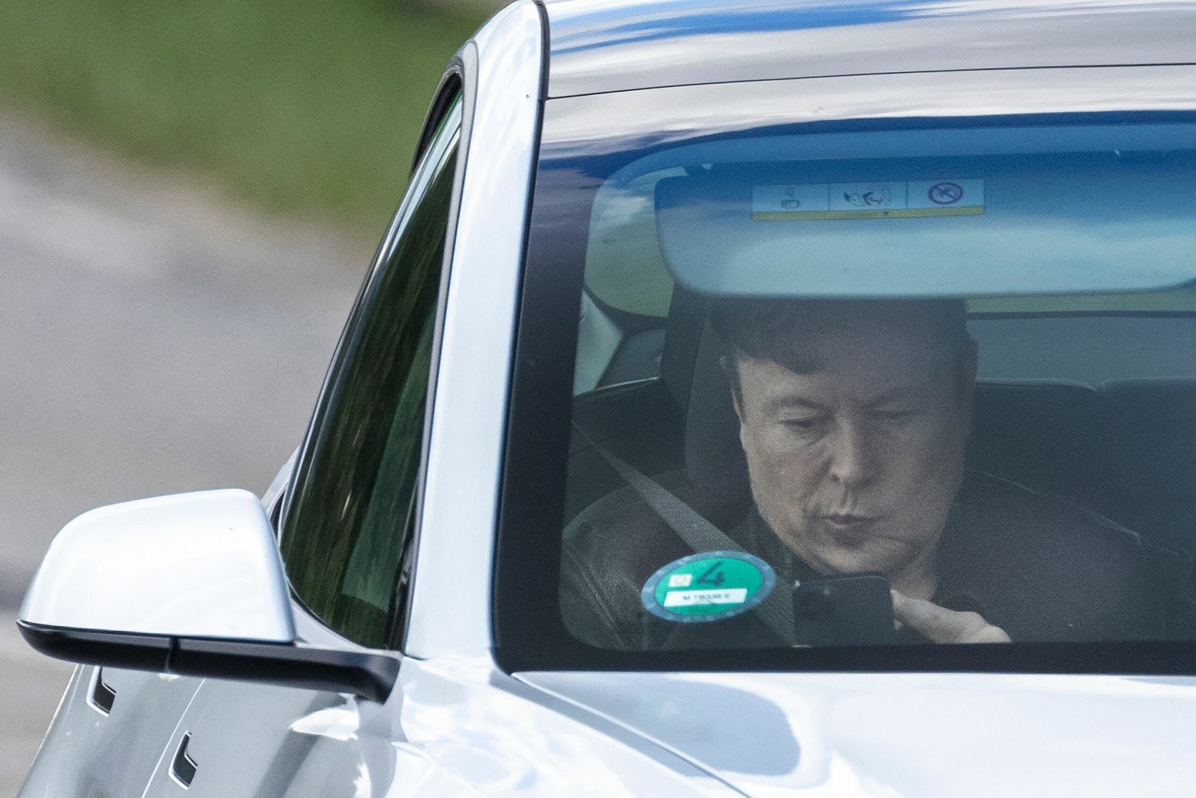 A person is in a car, looking down at a smartphone, with eyes partially closed.