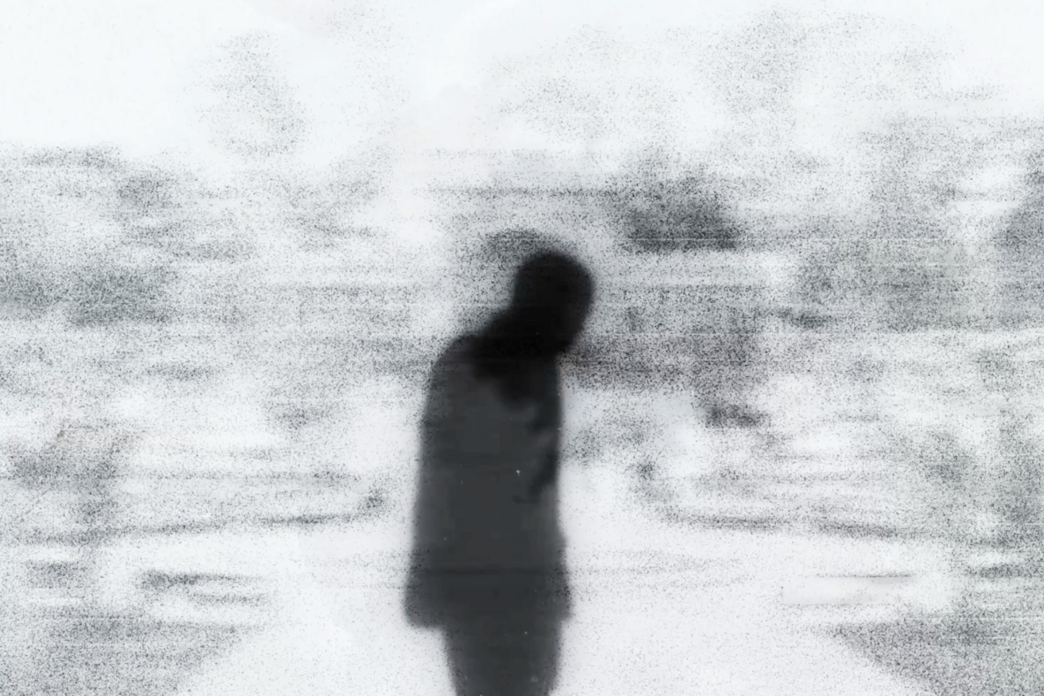 A blurry, grainy black-and-white figure of a person stands with head bowed against a foggy, indistinct background.