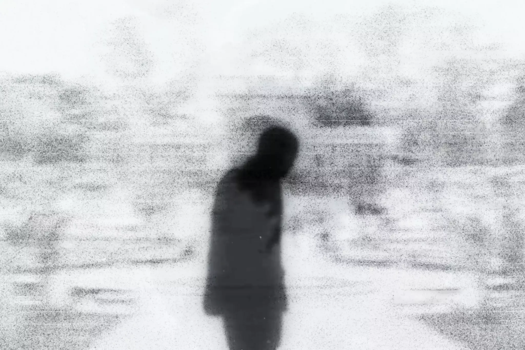 A blurry, grainy black-and-white figure of a person stands with head bowed against a foggy, indistinct background.