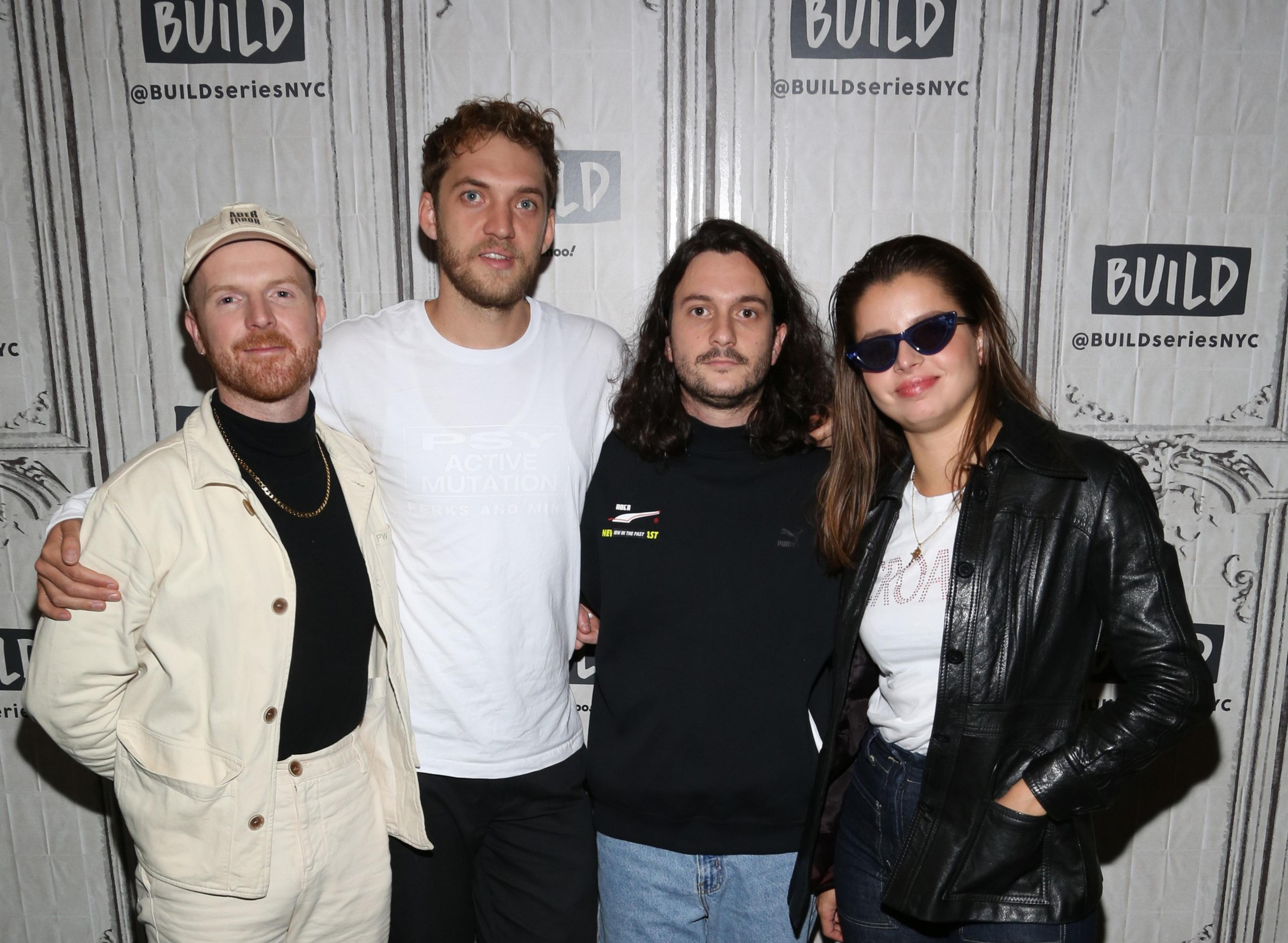 Four people stand close together against a backdrop with "BUILD @BUILDseriesNYC" logos, smiling, with one woman wearing sunglasses and a black leather jacket.