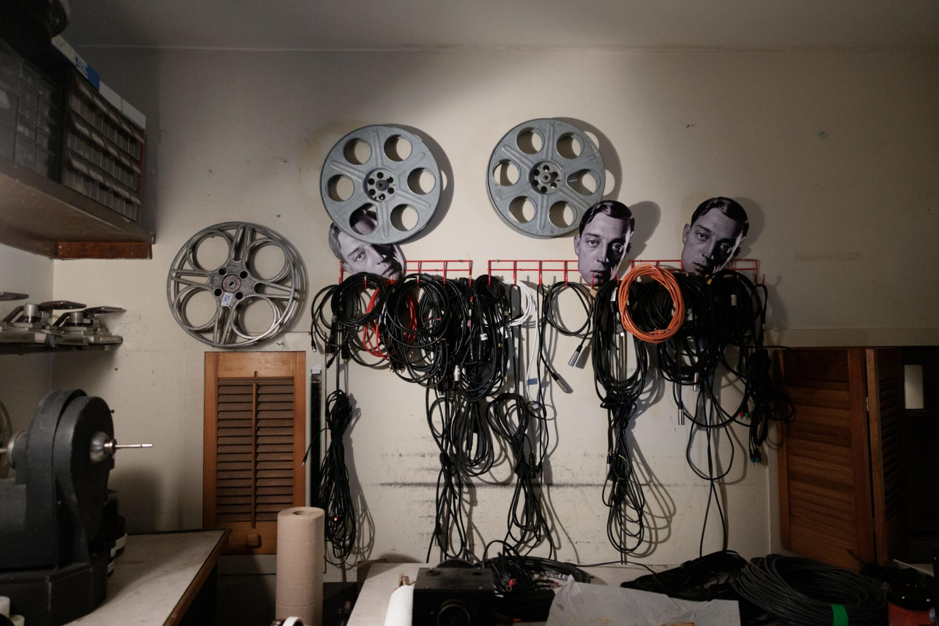 Three large film reels mounted on a wall serve as holders for numerous coiled cables, with cutout faces of a man placed among them.