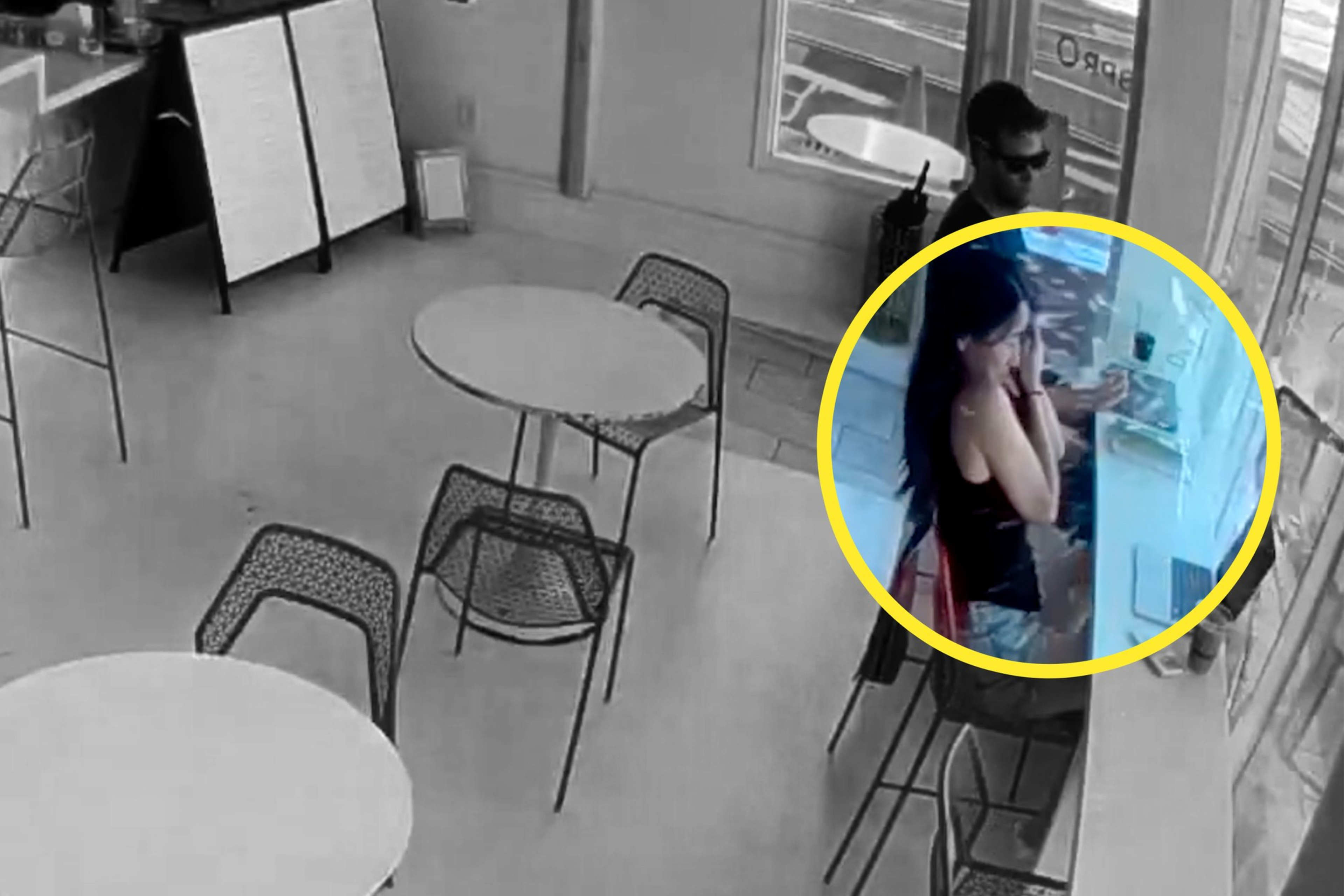 The image shows a mostly empty cafÃ© with a few tables and chairs. A highlighted section focuses on a woman using a laptop near a window, with a man standing behind her.