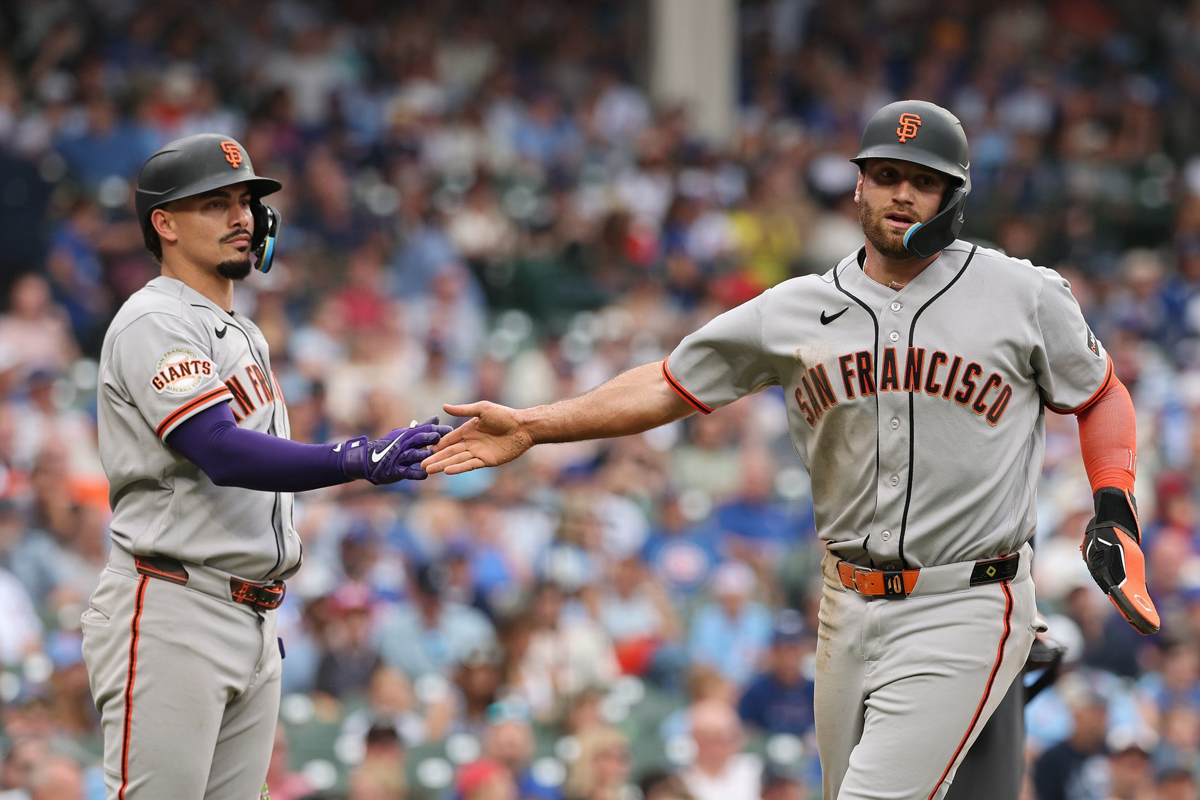 Two San Francisco Giants baseball players wearing helmets and gray uniforms are giving each other a low five during a game.