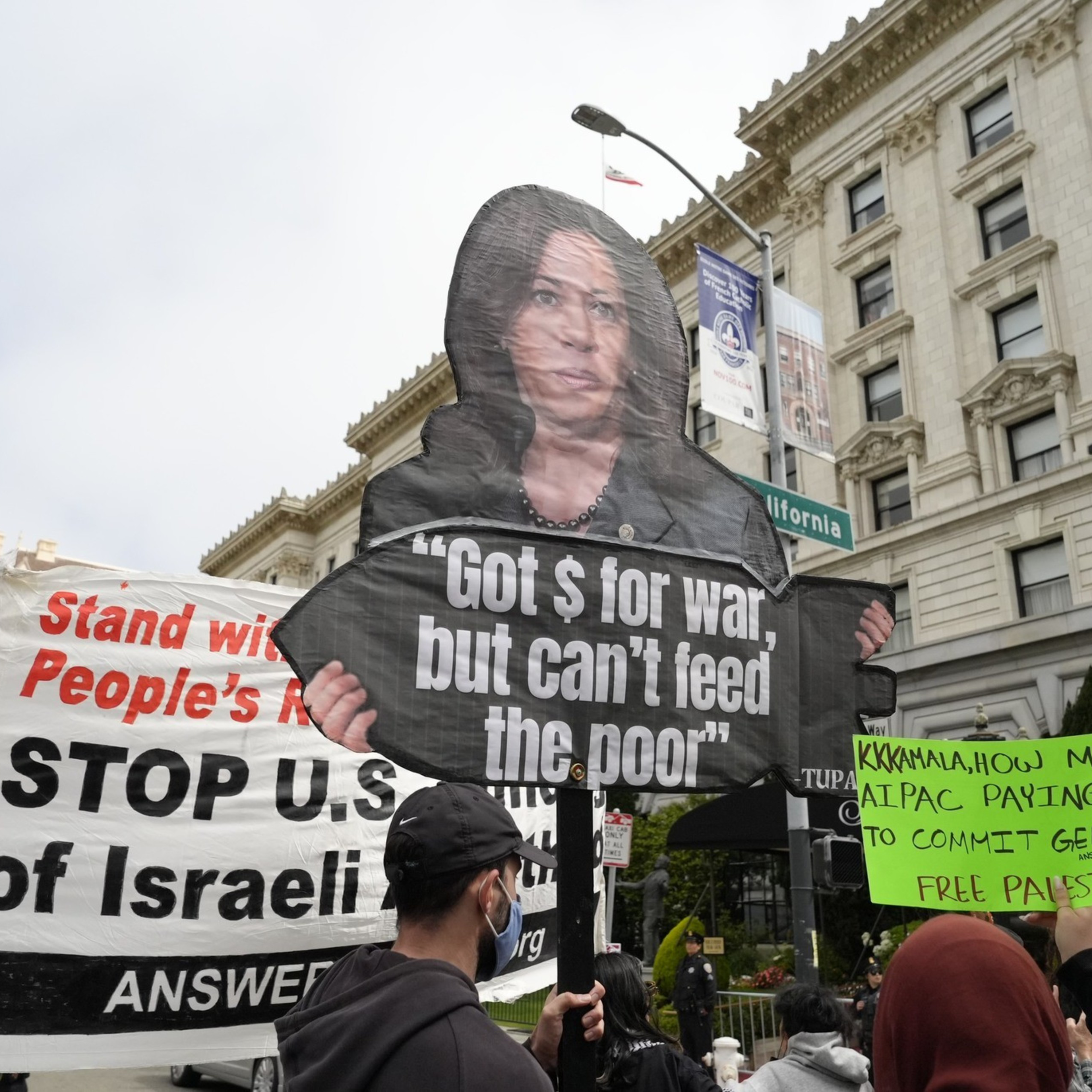 Protesters hold various signs, including one with a picture of a person and the text &quot;Got $ for war, but can't feed the poor&quot; and others showing support for Palestine.