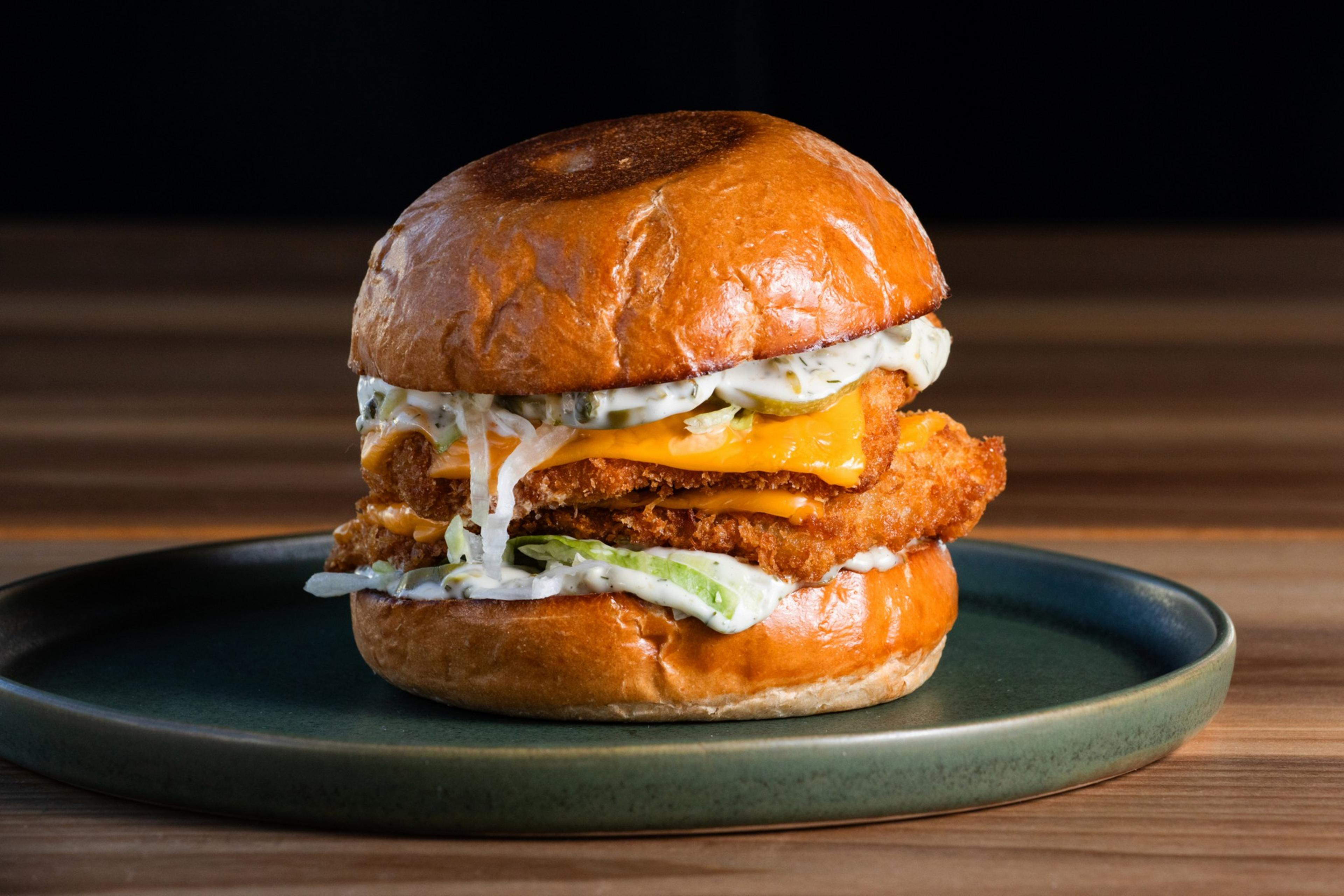 A crispy chicken sandwich with melted cheese, creamy sauce, and lettuce is on a green plate with a wooden table background.