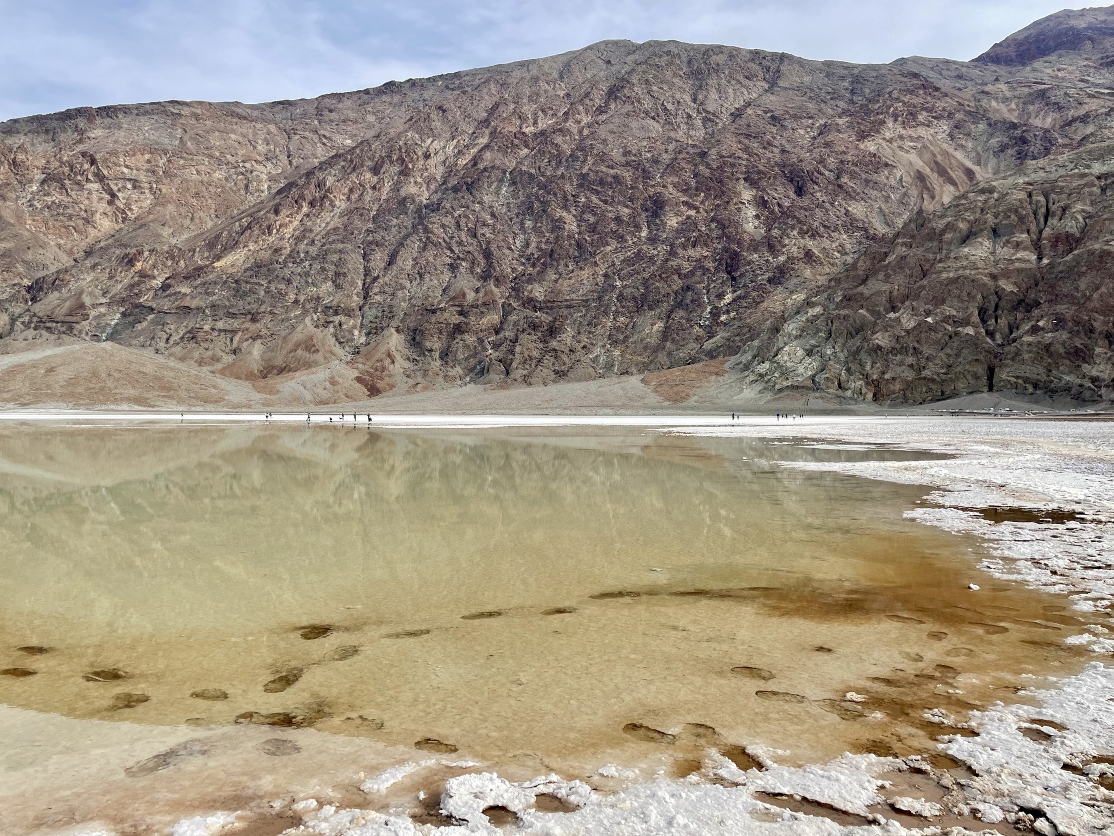 Footsteps are seen below the surface of a clear lake in a desert. 