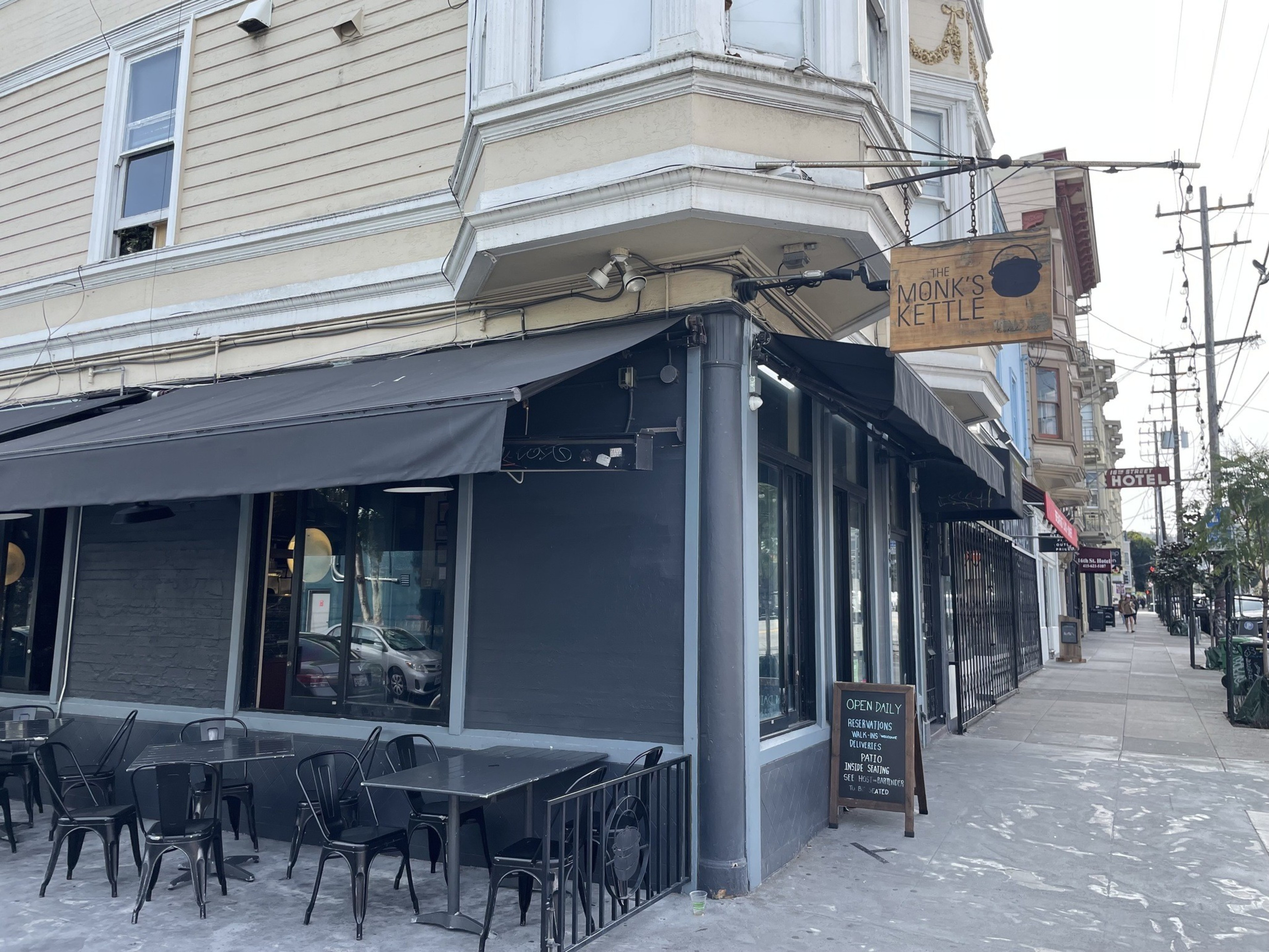 A corner street view with "The Monk's Kettle" pub, sidewalk seating available, and an "Open Daily" sign.