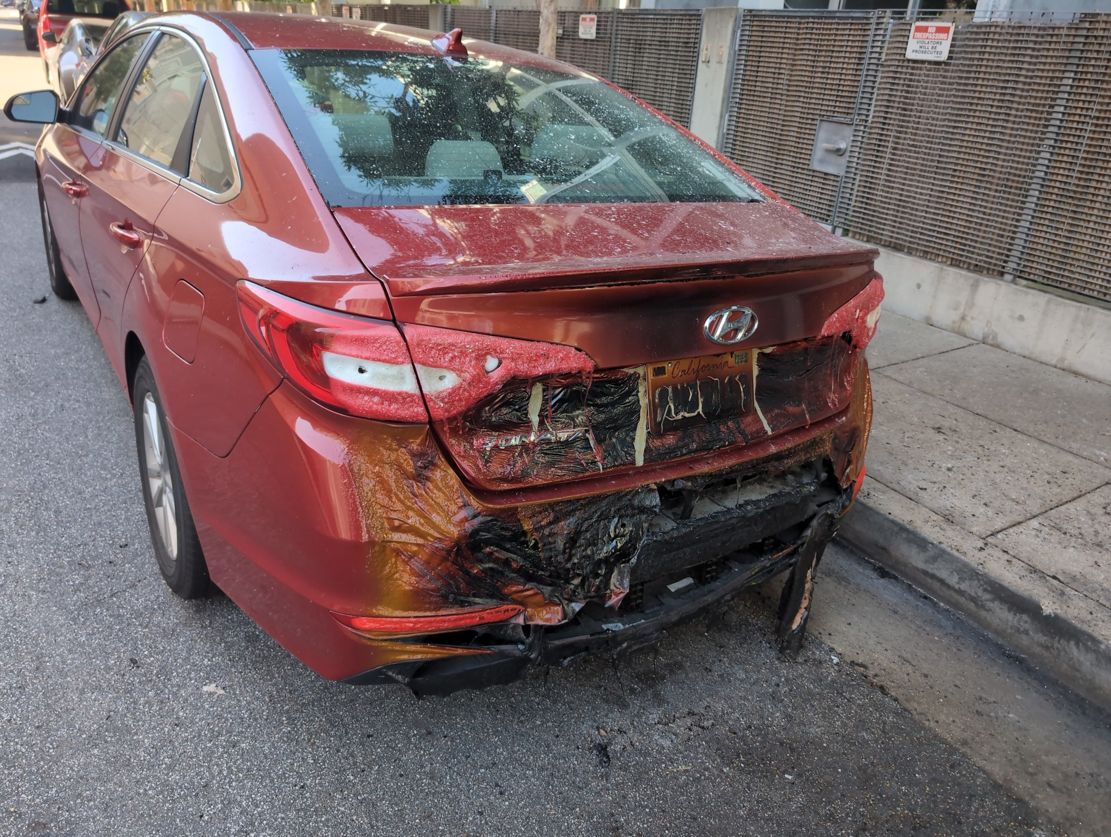 A parked vehicle's rear bumper is blackened by a vehicle fire a day earlier