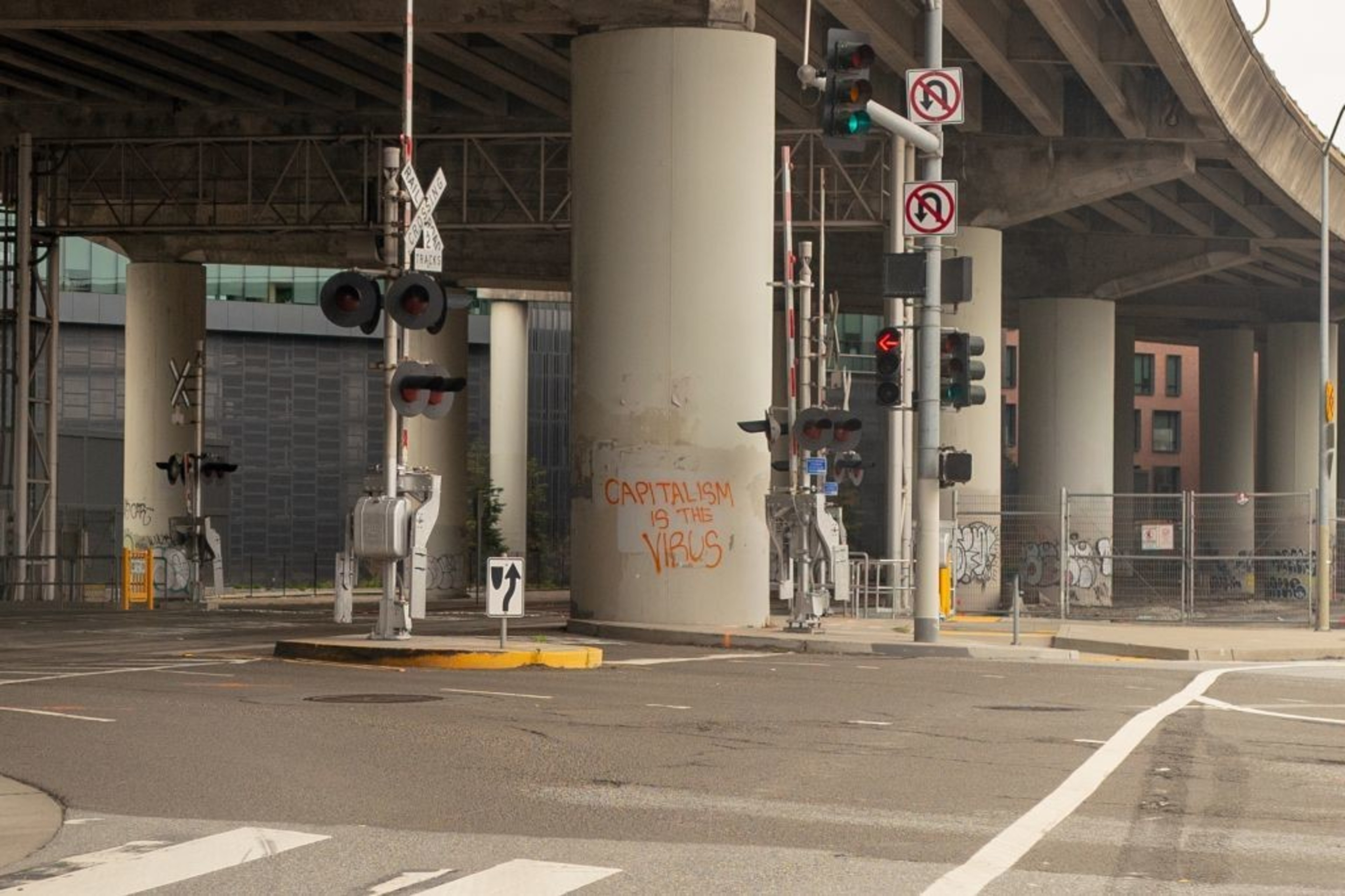 Graffiti reading &quot;capitalism is the virus&quot; is sprayed in orange-colored paint on a concrete pillar supporting a highway overpass near train tracks in San Francisco on April 6, 2020, during the early days of the Covid-19 pandemic.