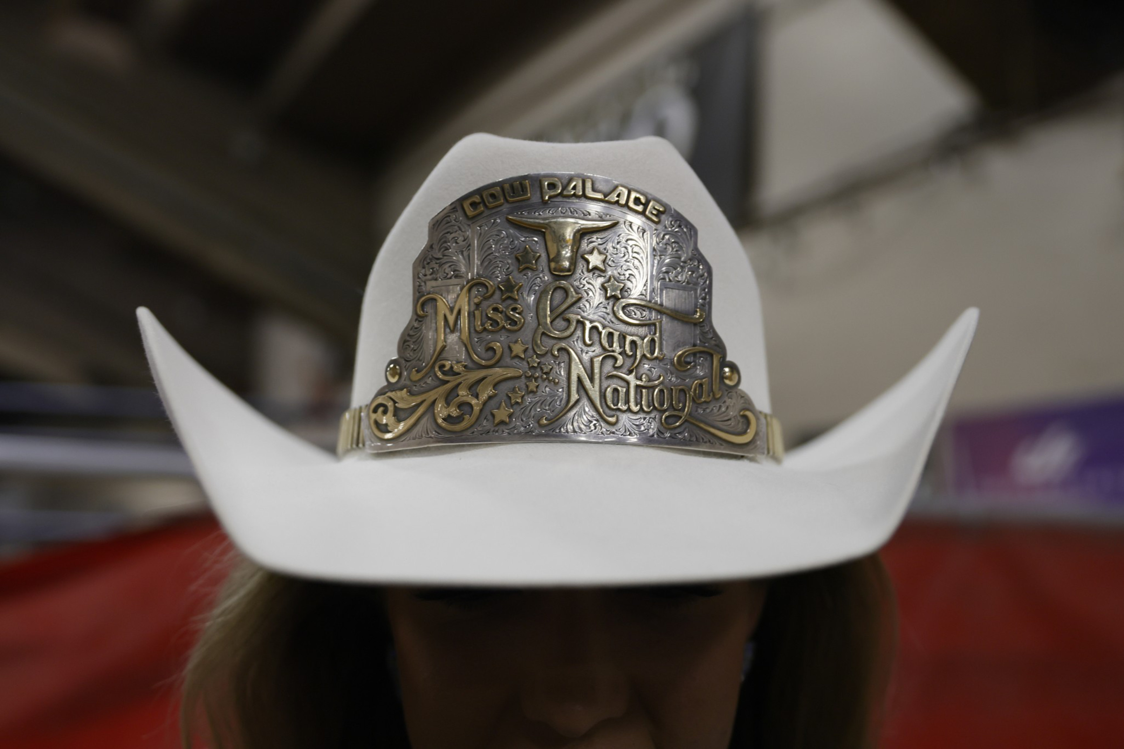 A white cowboy hat with a large silver and gold plaque reading “Cow Palace Miss Grand National” featuring a longhorn skull and western motifs.