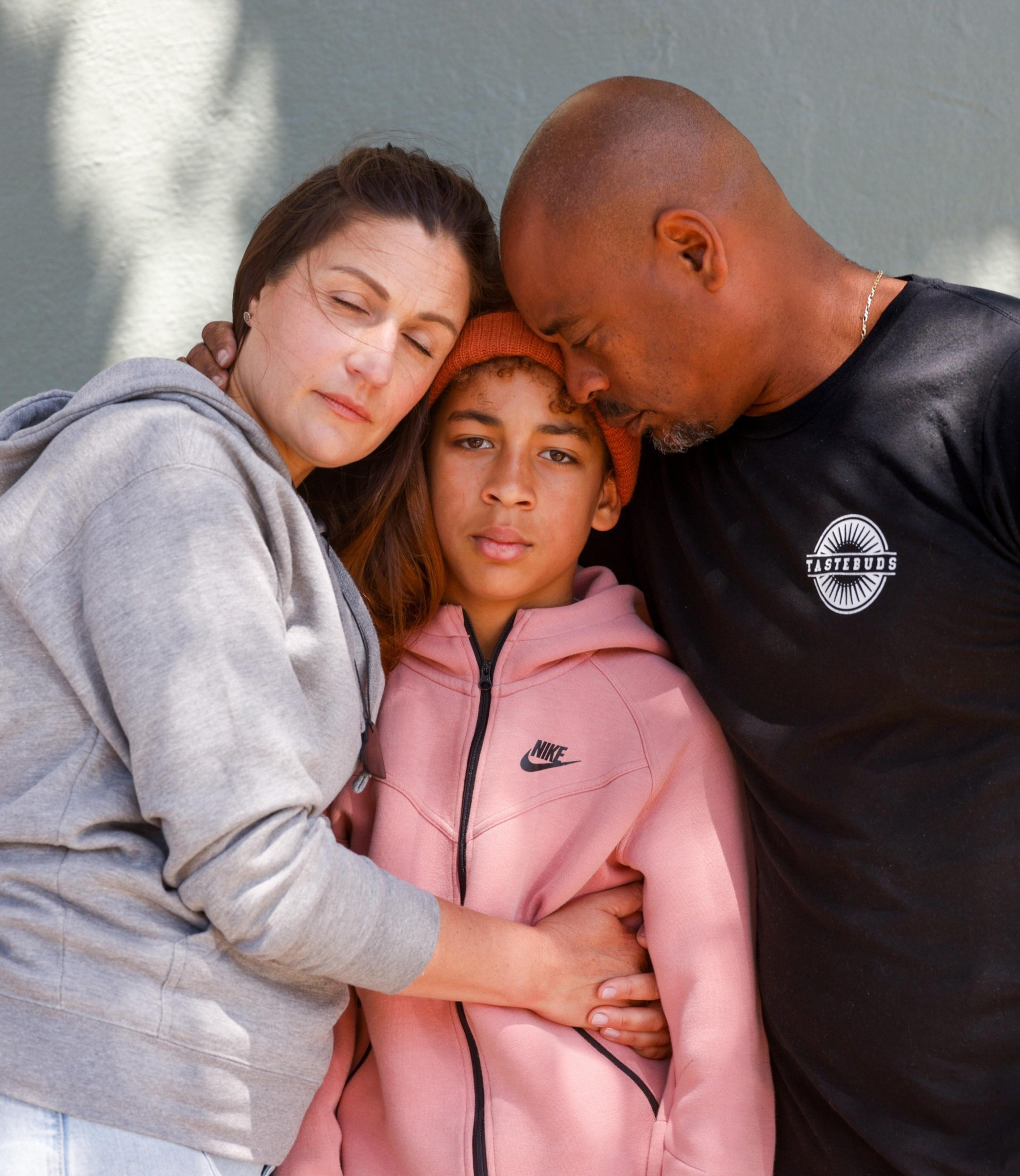 A family of three embraces lovingly, with the mother and father tenderly leaning their heads against their child's.