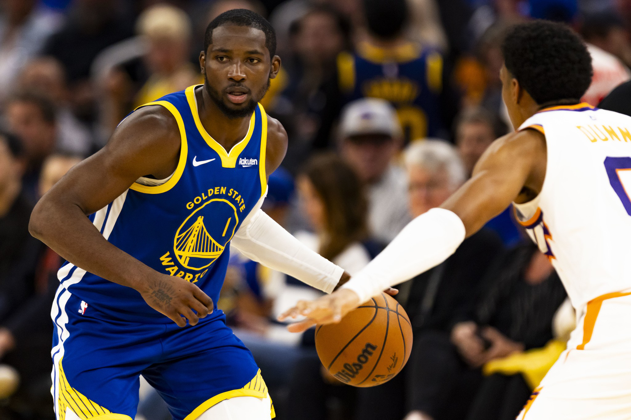 A Golden State Warriors player dribbles the basketball while guarded closely by a Phoenix Suns player during a game.