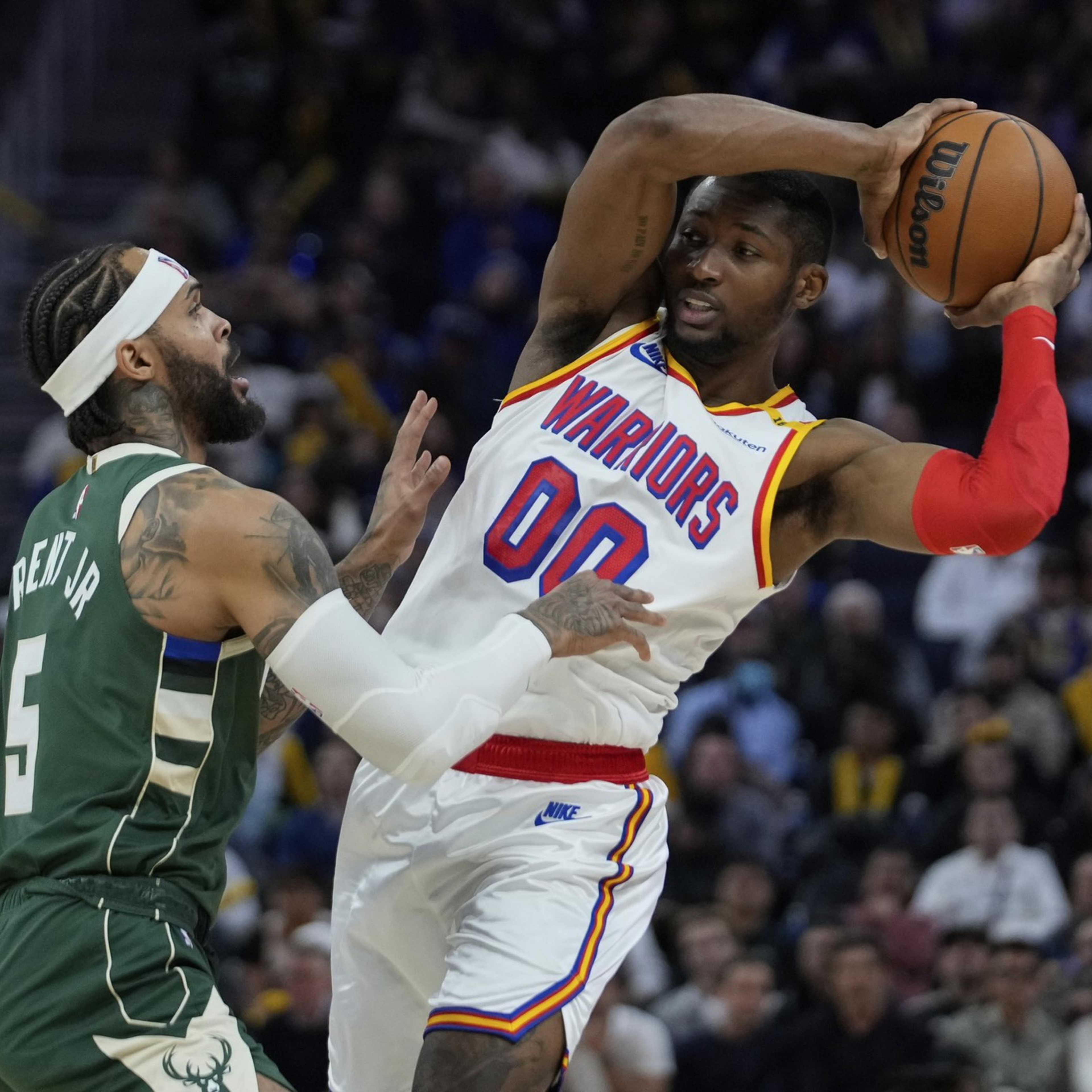 A Warriors player with the ball fends off a defending Bucks player wearing number 5 during an intense basketball game.