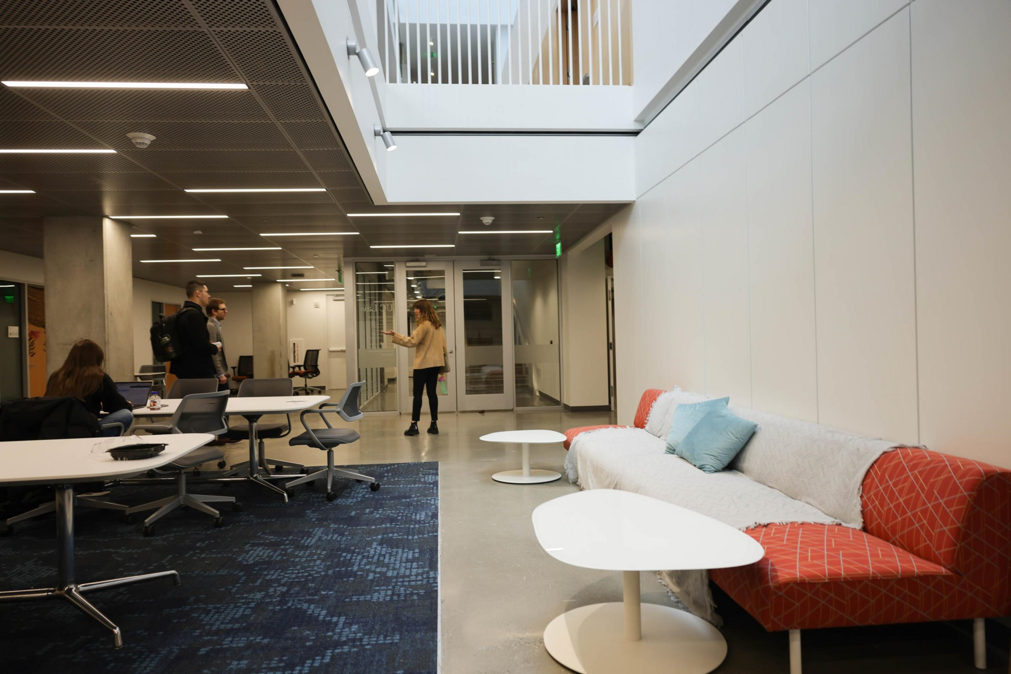 A modern office lounge with sofas, tables, people chatting, and a bright, airy design.
