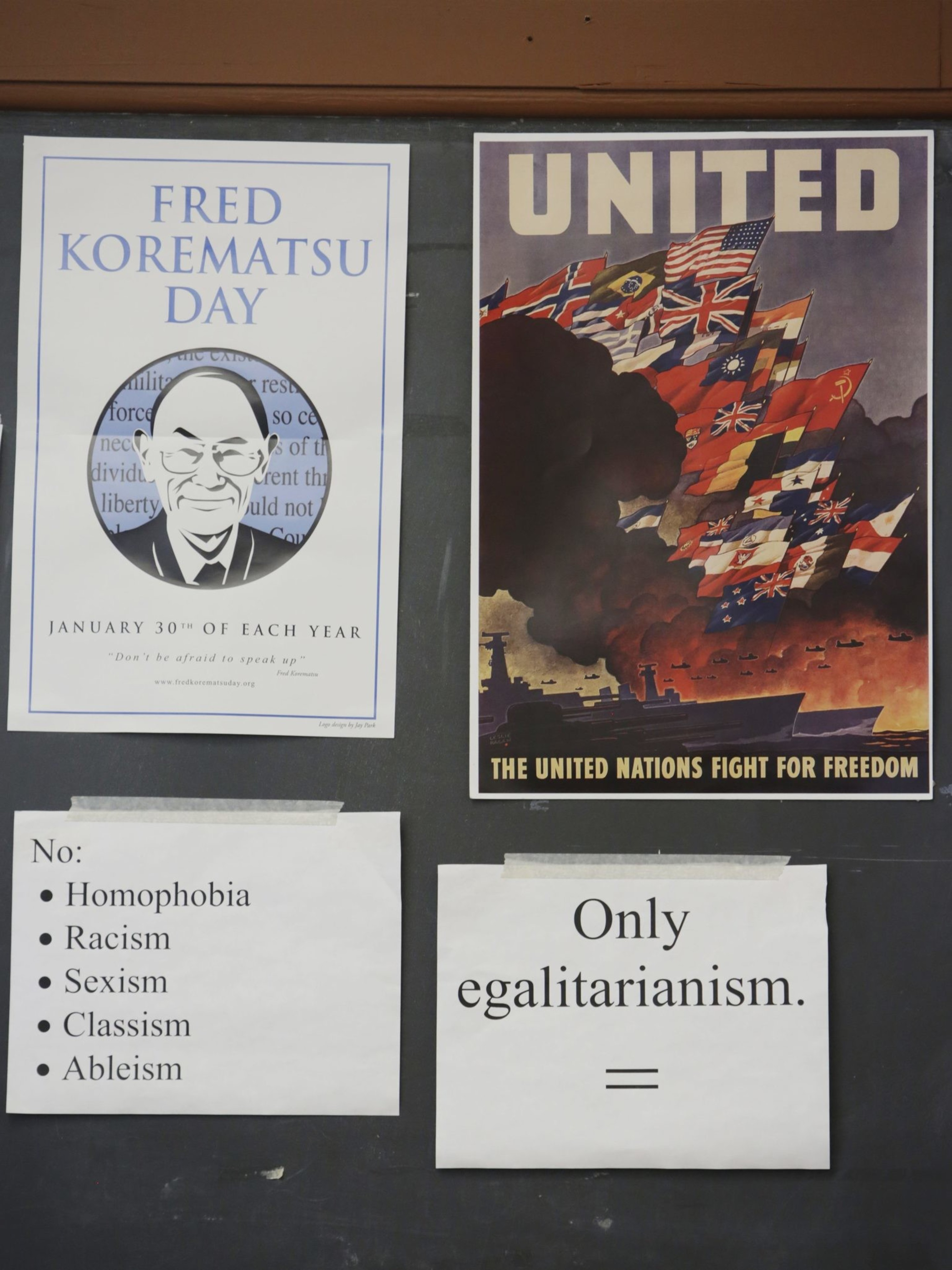 Two posters, one for Fred Korematsu Day, the other showing United Nations flags. Below are signs opposing discrimination and supporting egalitarianism.