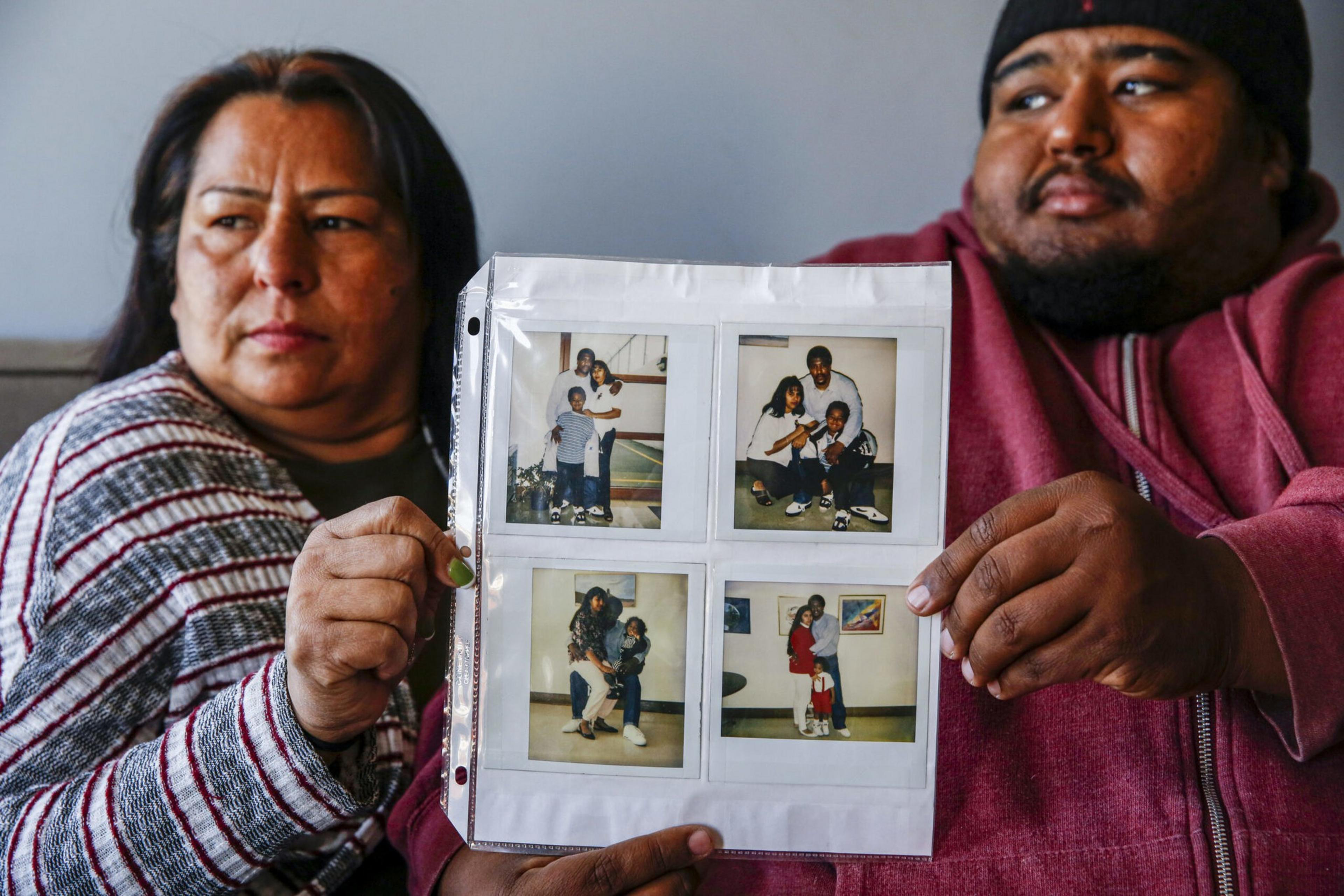 A woman and a man hold a plastic sheet with four old family photos featuring children and adults in casual settings.