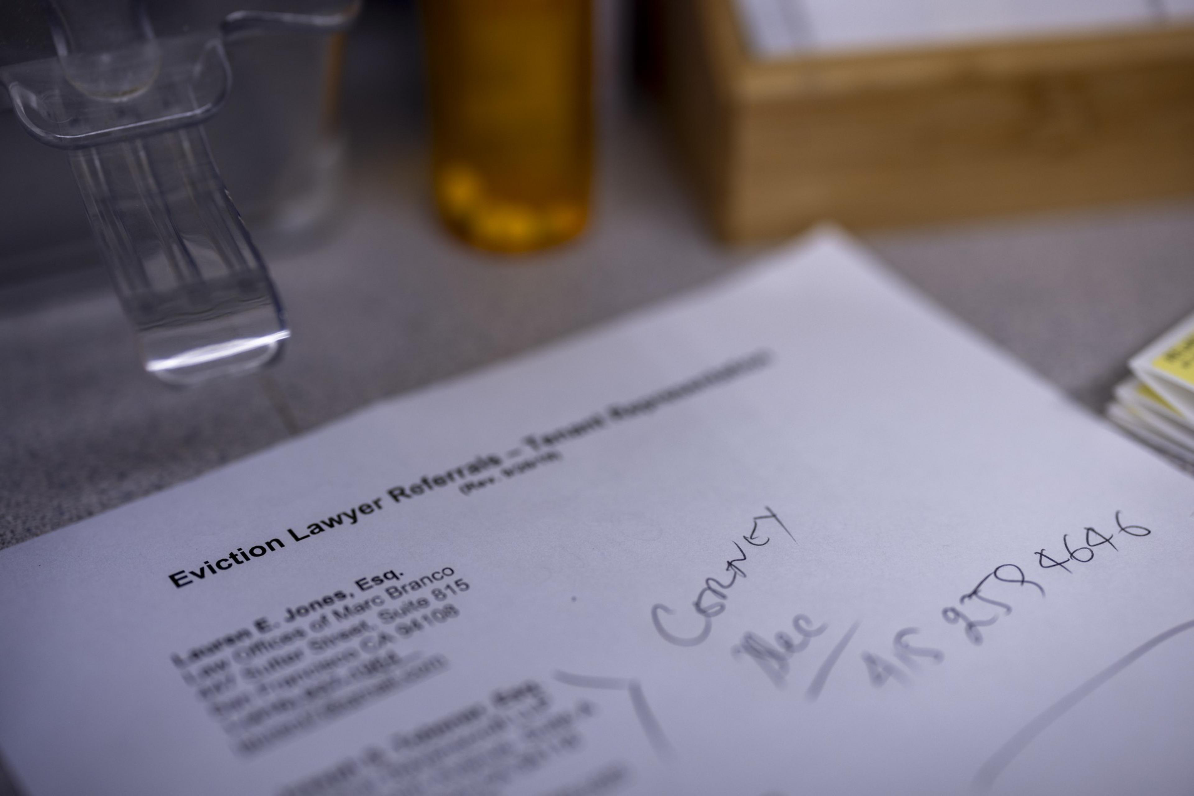 A paper titled &quot;Eviction Lawyer Referrals&quot; is on a table, with handwritten notes and contact information. Nearby, a prescription bottle and a wooden box are visible.