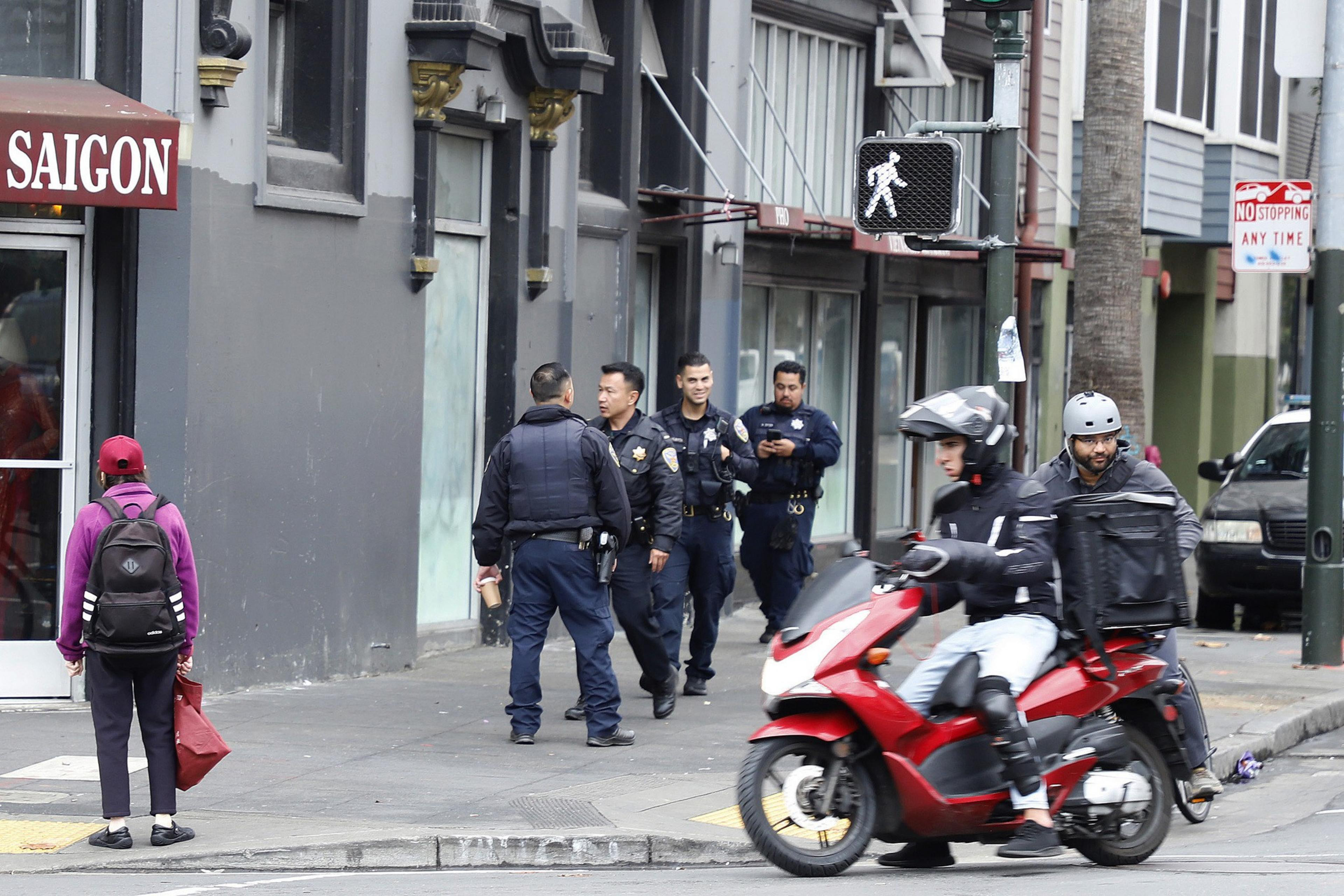 Four police officers walk down the street as cars pass by.