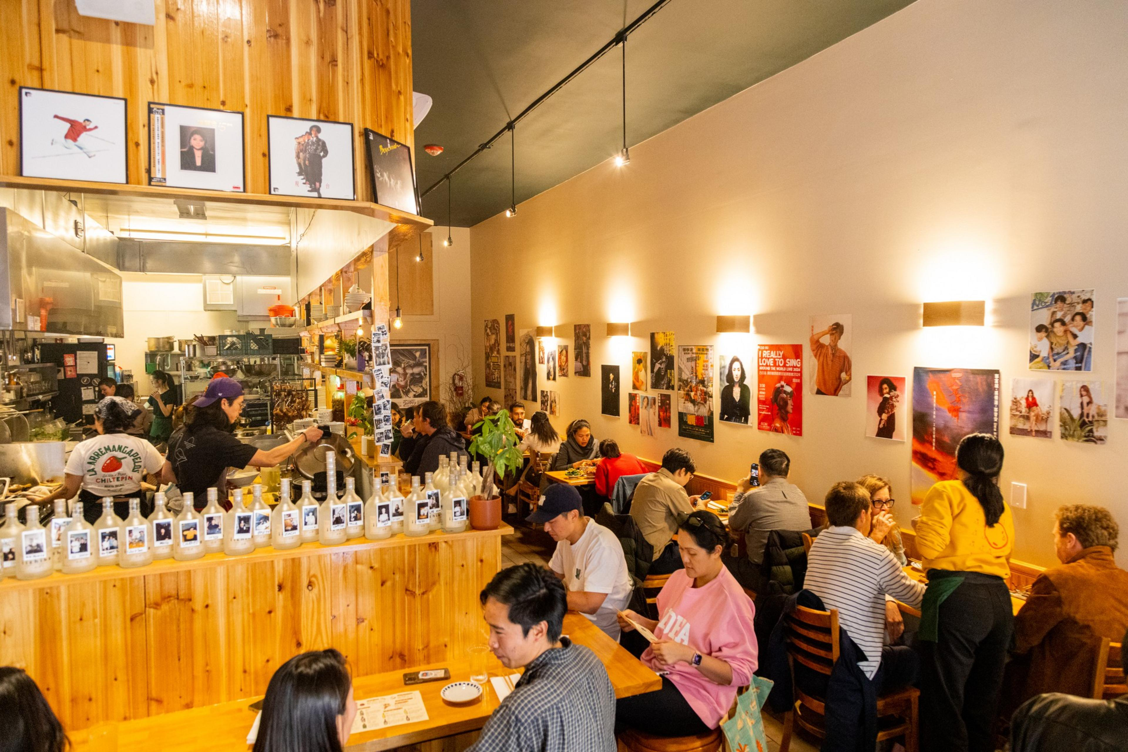 A busy café with wooden décor, patrons dining, posters on walls, and a barista at work.