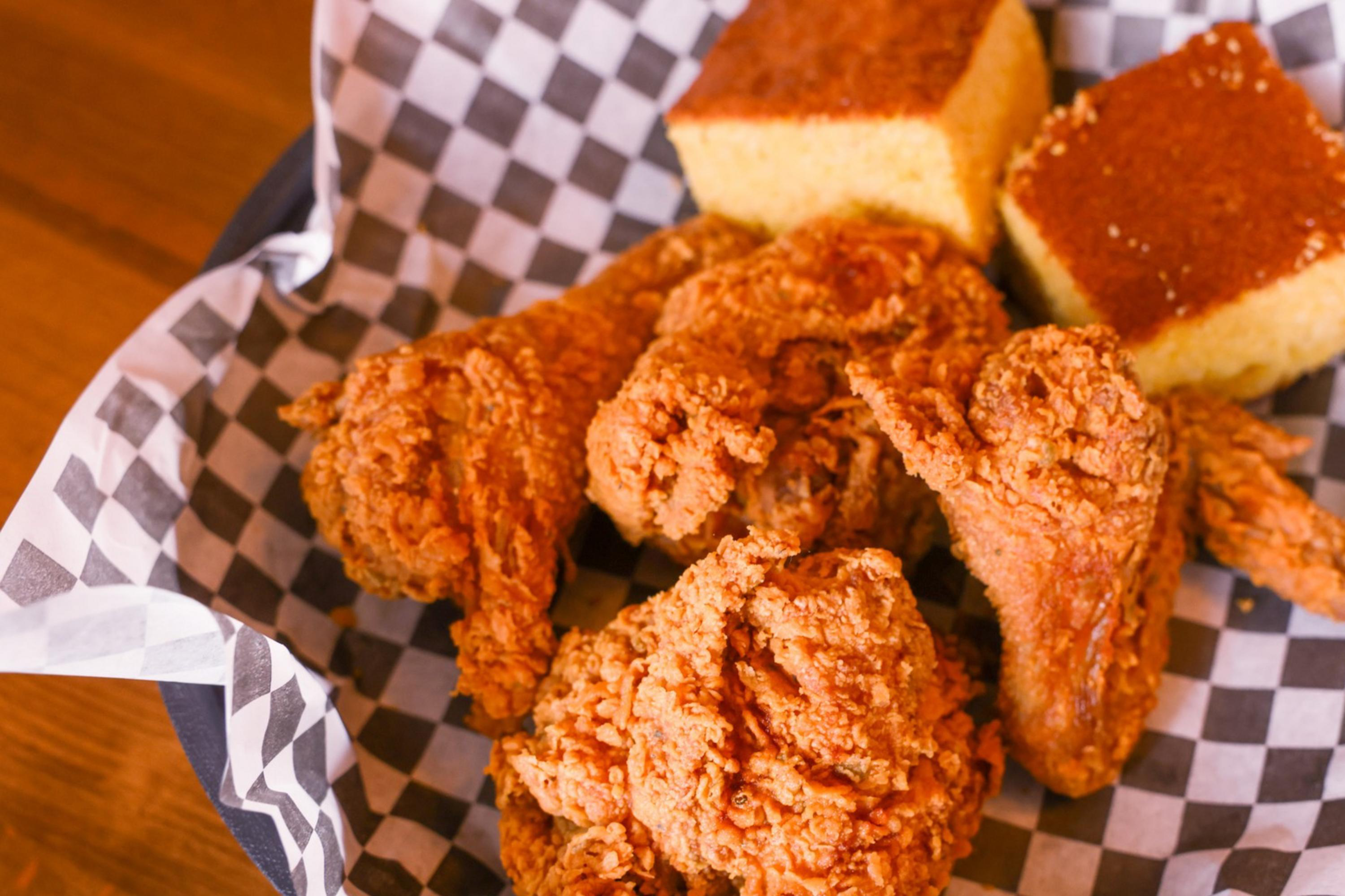 Fried chicken and cornbread in a basket with checkered paper; collard greens visible in the background.