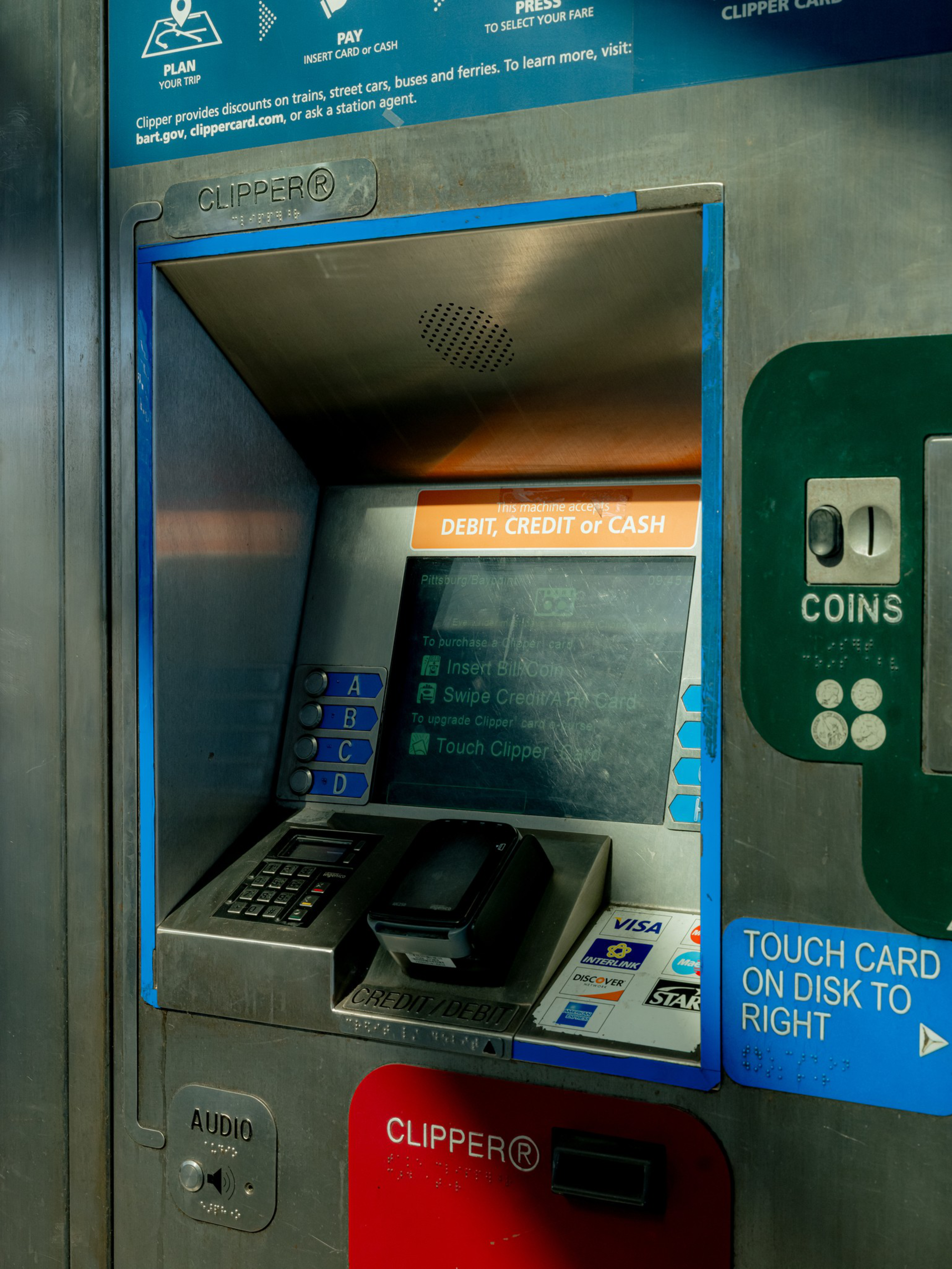 Ticket vending machine with a keypad, card reader, coin slot, and touchscreen for paying with debit, credit, or cash. Instructions and payment logos are visible.