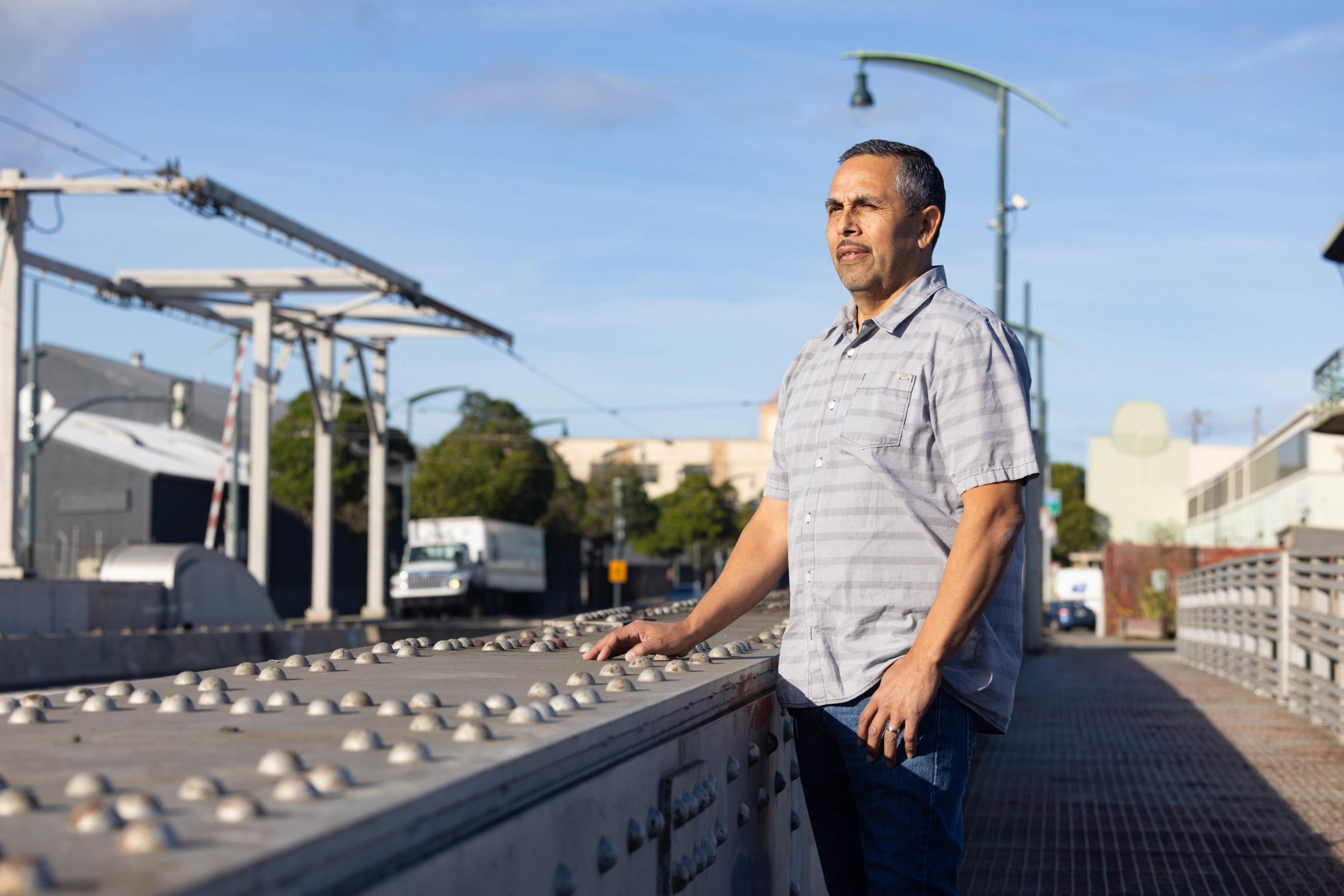 A man a gray bottom shirt poses for a portrait along a bridge