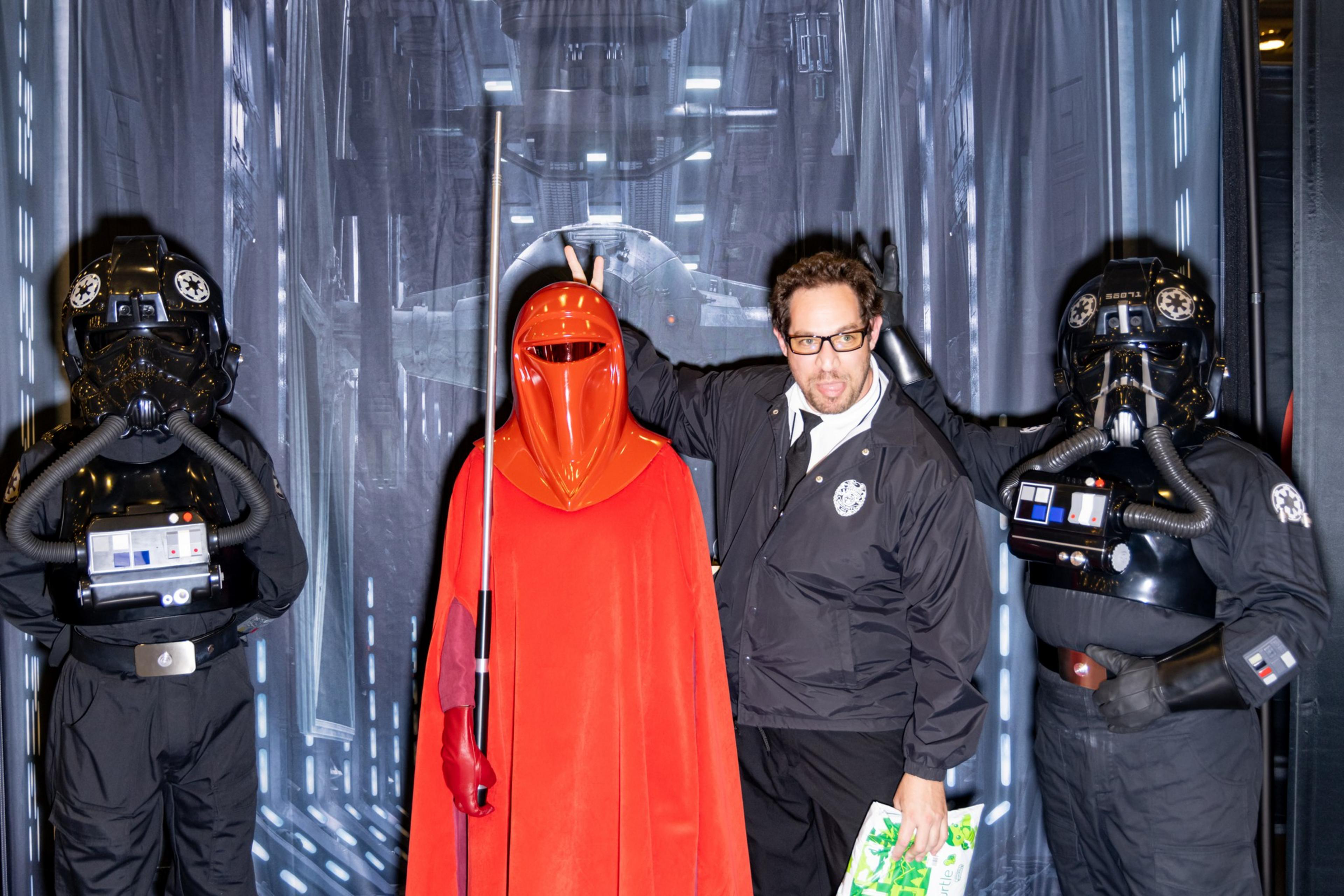A person stands with two stormtrooper cosplayers and an Imperial Guard from Star Wars. They pose playfully against a backdrop of a spaceship interior.