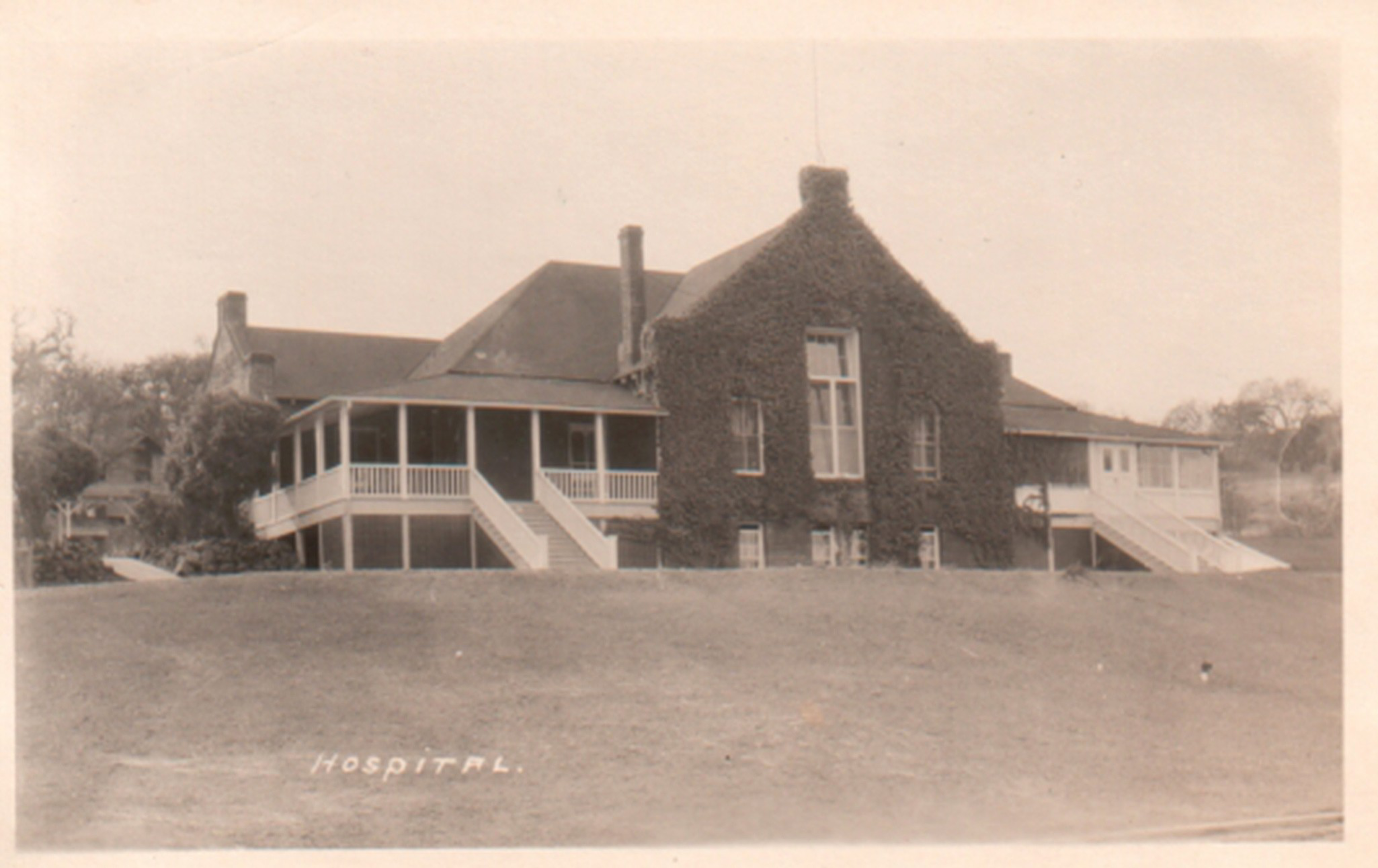 A large old building covered in ivy with multiple porches and staircases sits on a grassy hill, labeled "Hospital."