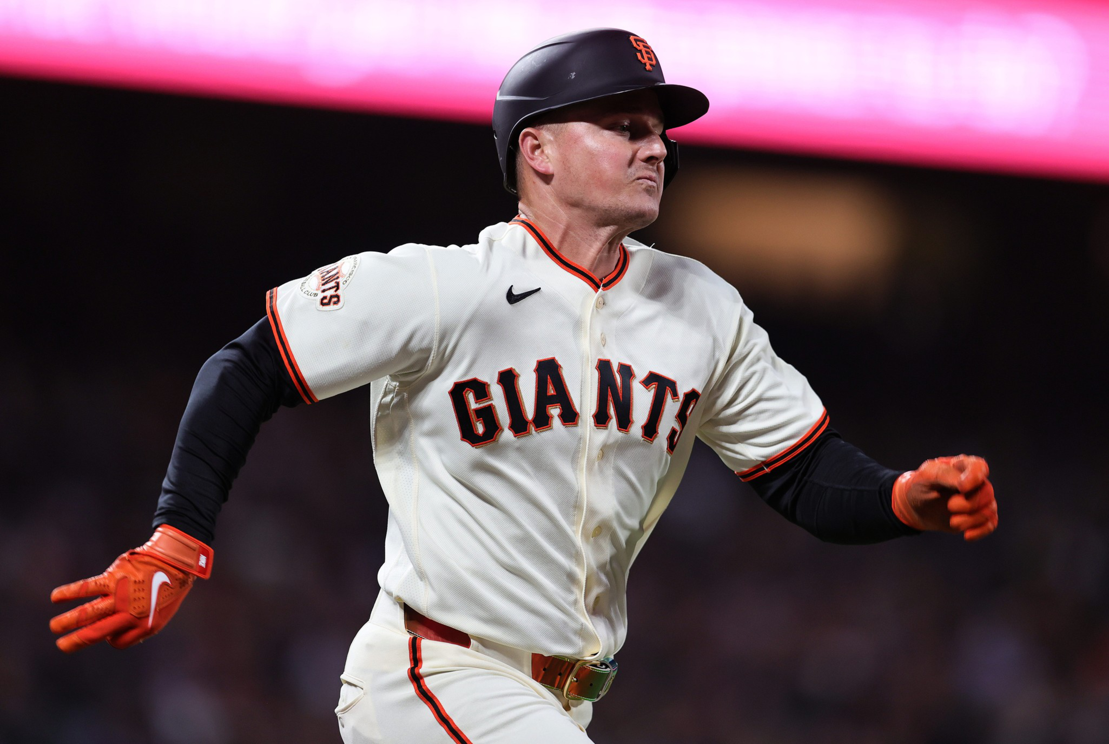 A baseball player in a San Francisco Giants uniform is running intensely, wearing an orange glove and black helmet.