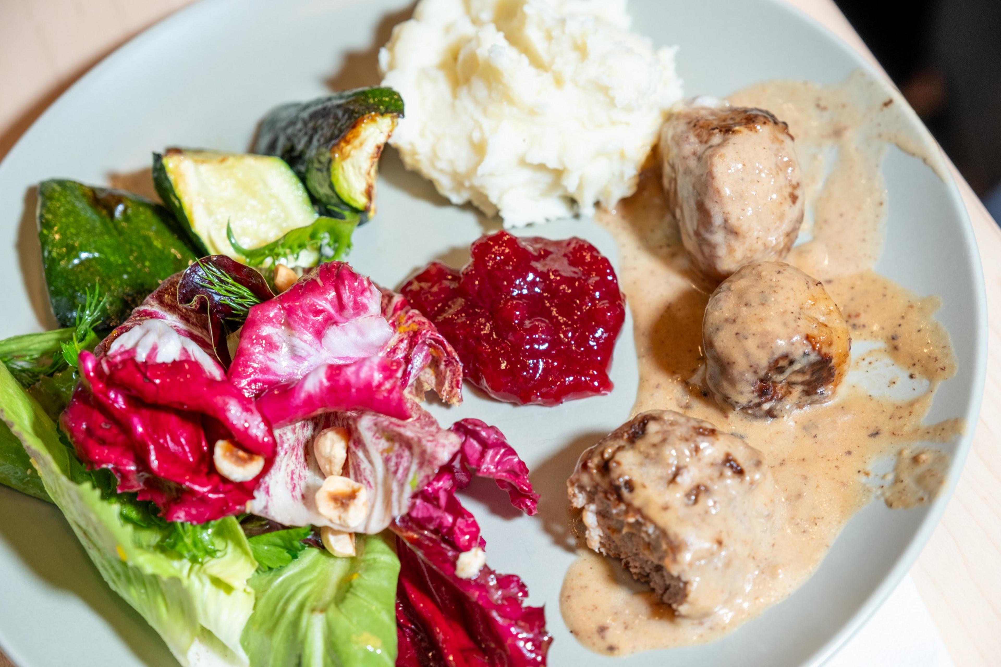 The image shows a plate with meatballs in sauce, mashed potatoes, cranberry sauce, roasted zucchini, and a colorful salad with nuts.
