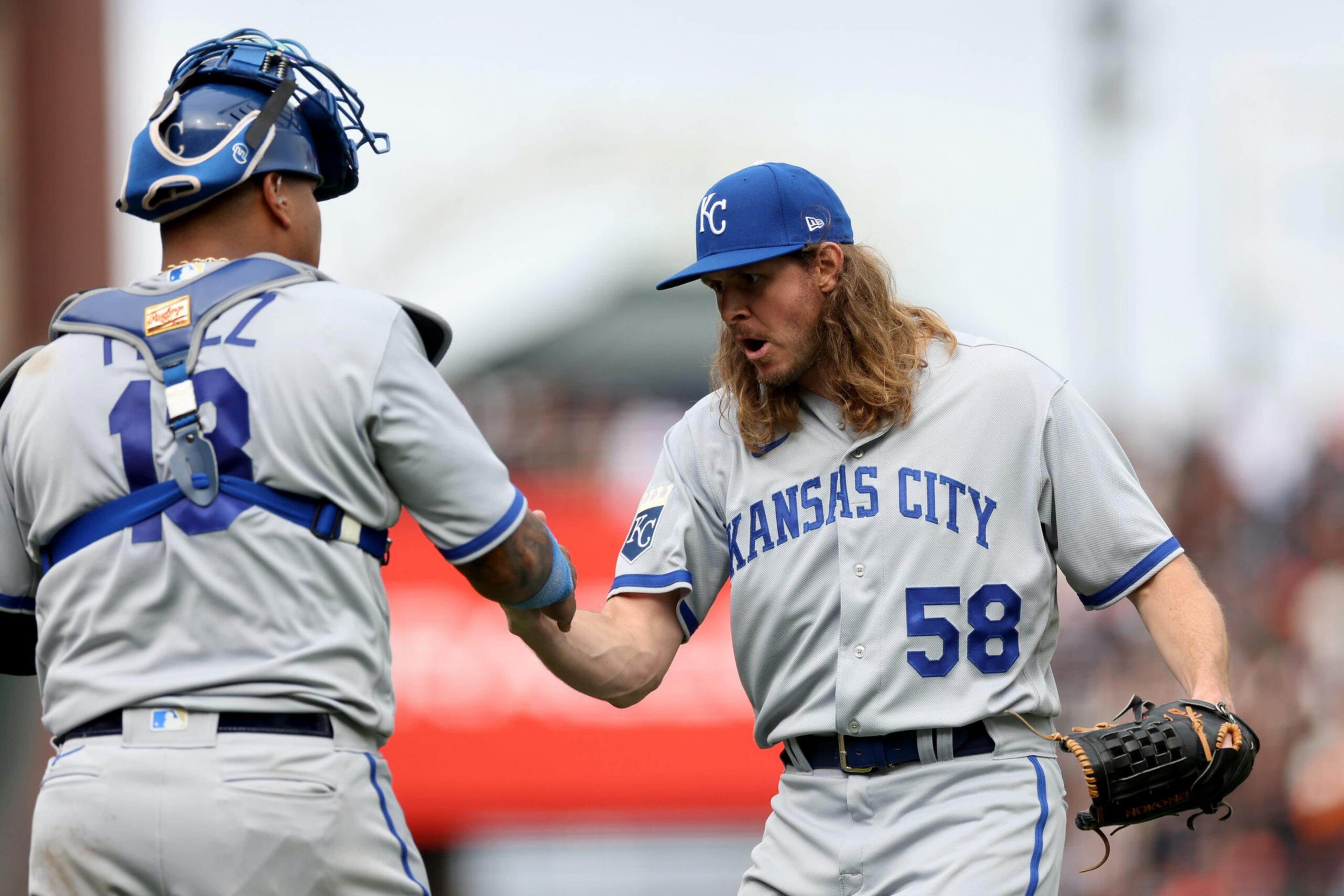 Two Kansas City Royals baseball players are fist-bumping during a game, with one wearing catcher's gear and the other holding a glove.
