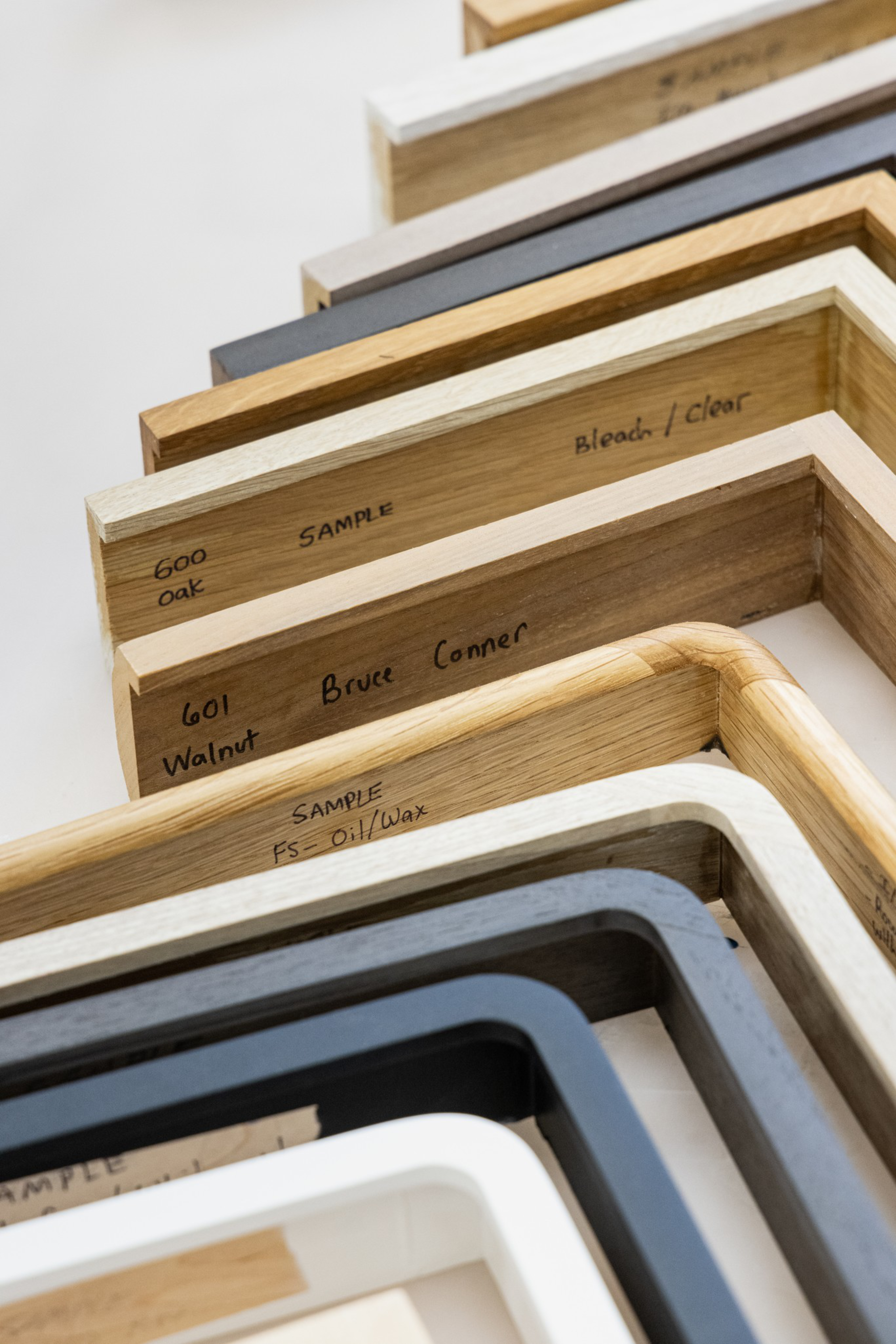 Several angled wooden and painted frame samples labeled with wood types and finishes are arranged in a staggered overlapping row.