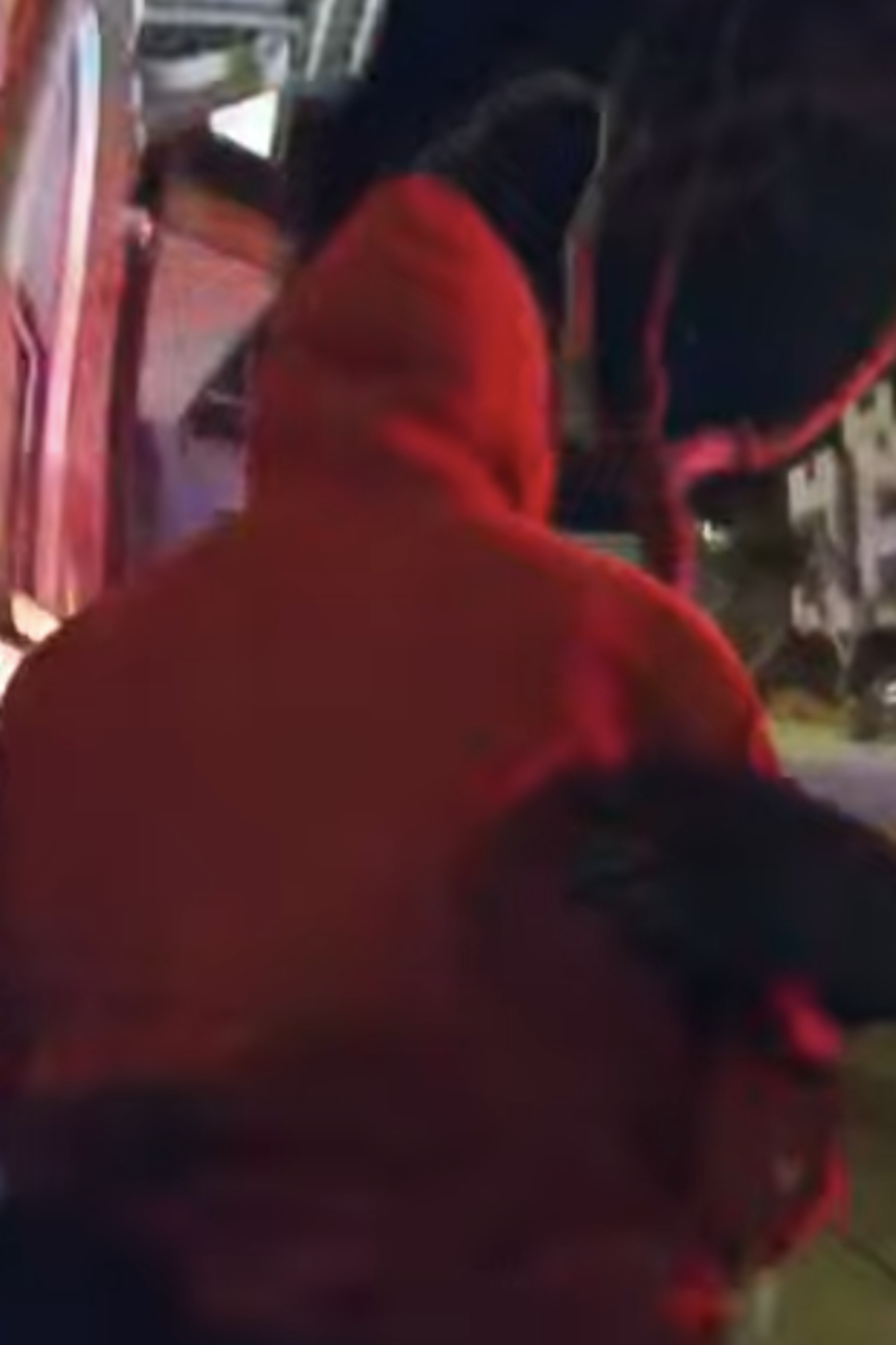 A police officer wearing black gloves holds the arm of a person in a red hoodie during a nighttime street interaction.