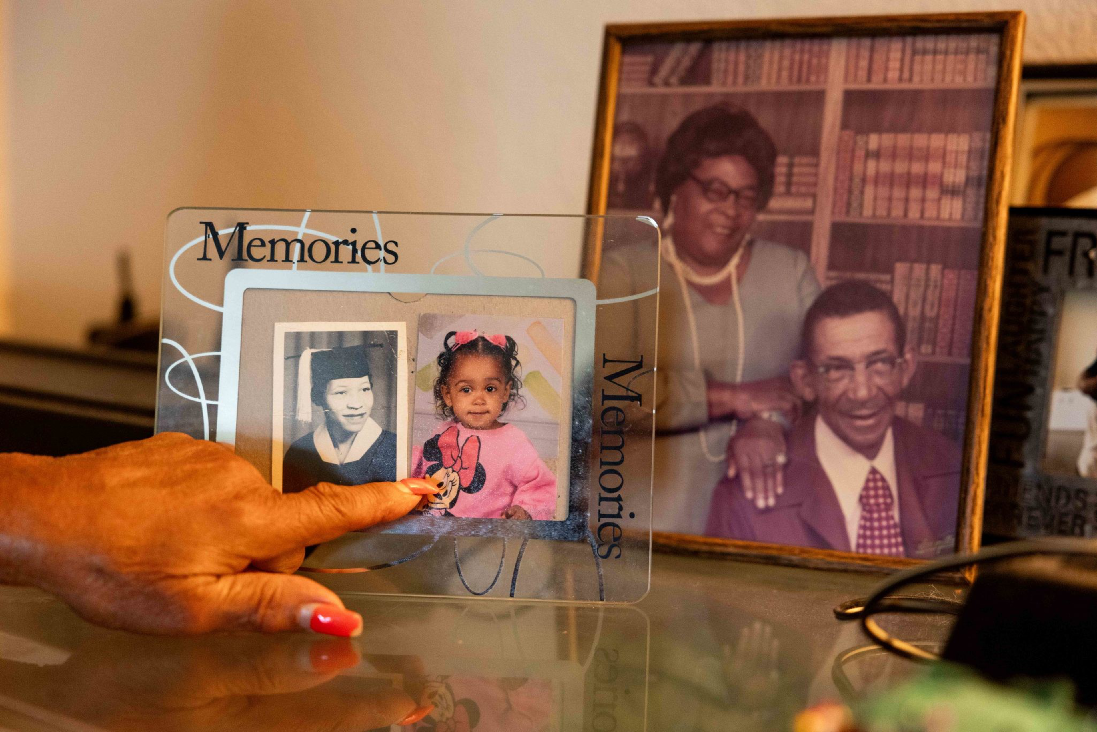 A hand with painted nails points at a child’s photo in a glass frame with two pictures, one of a child and one of a woman in graduation attire.