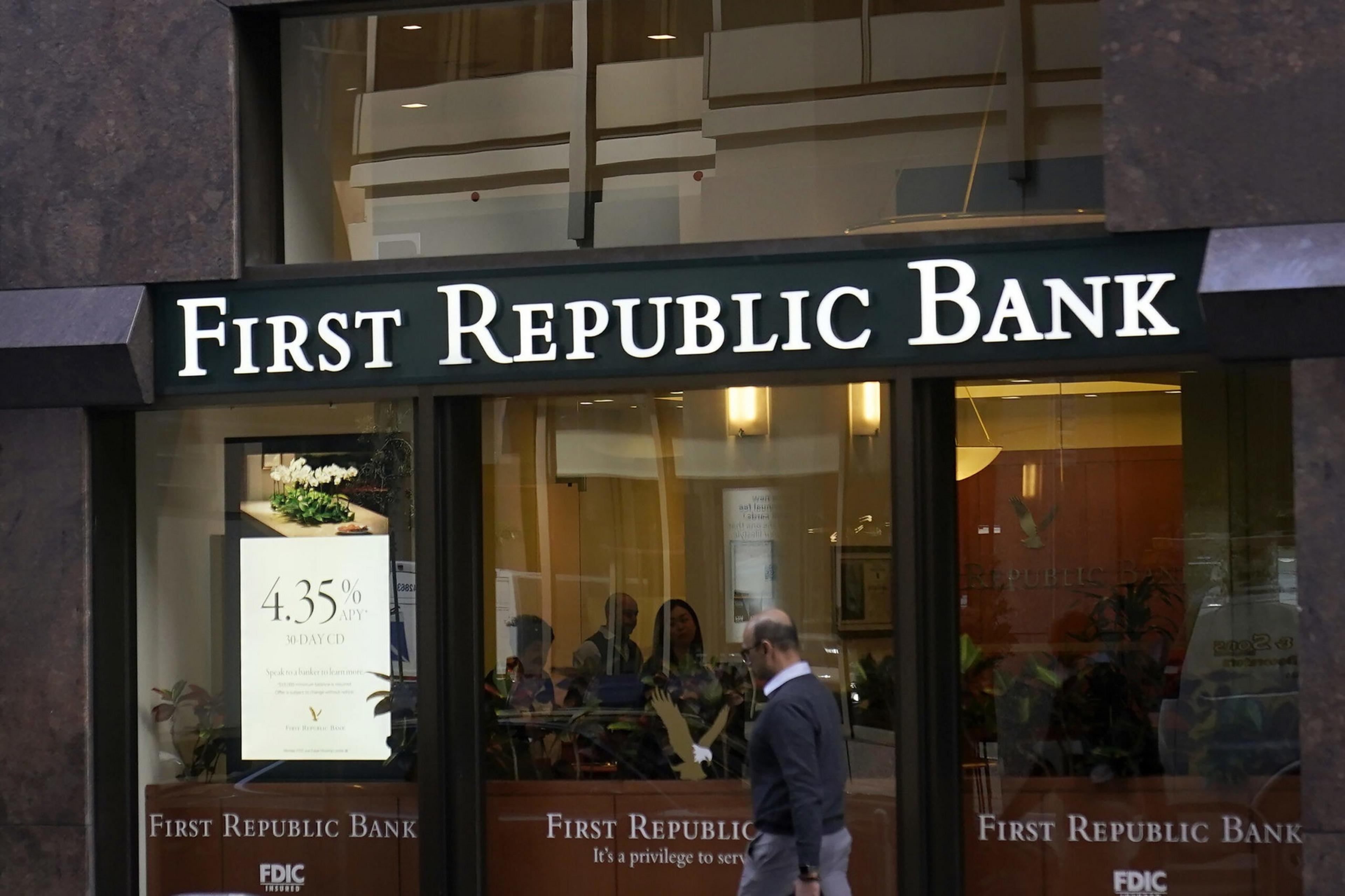 A man walks past the glass entrance of First Republic Bank, which displays its name and a poster advertising a 4.35% APY rate.