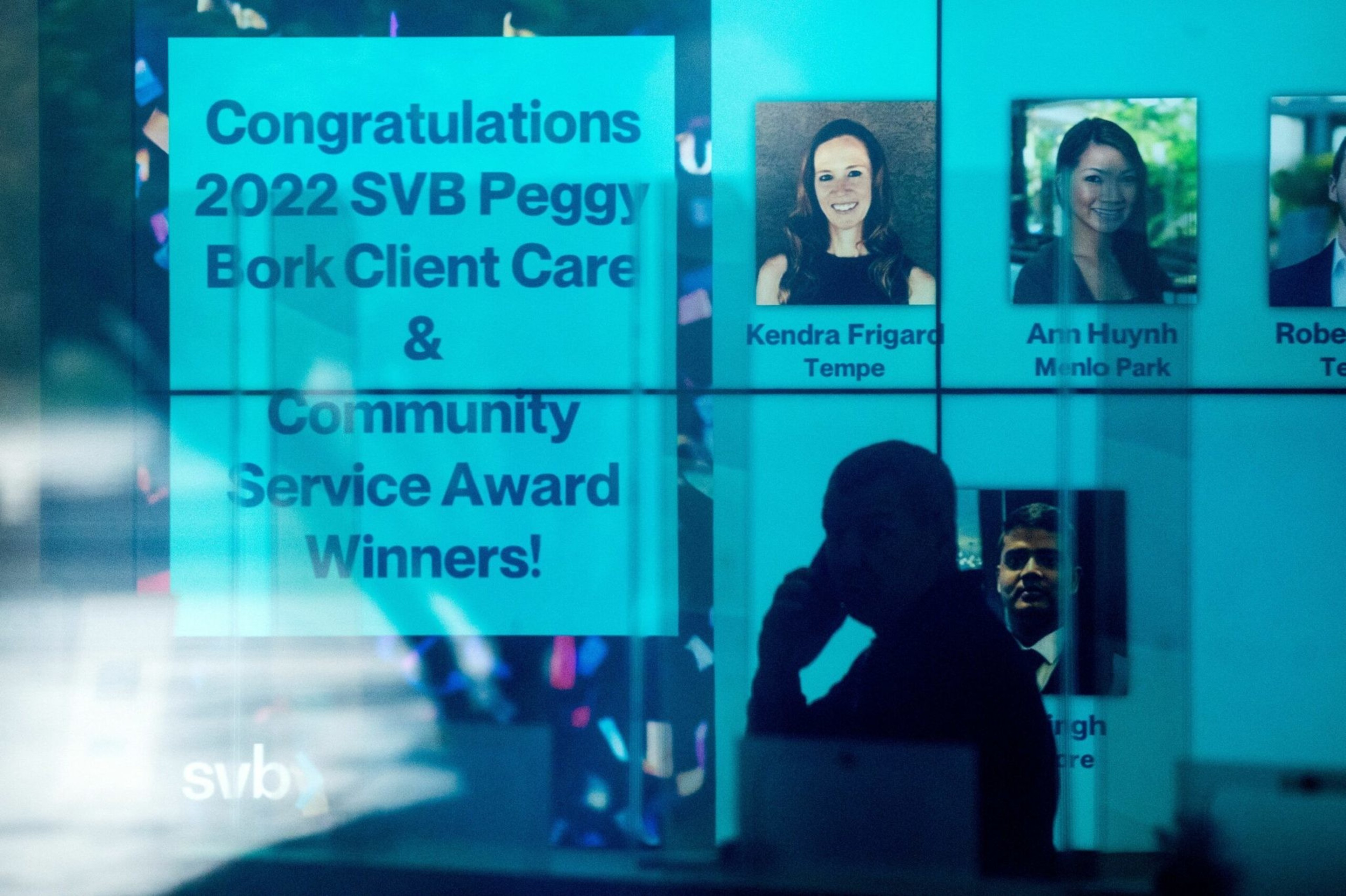 A screen displays "Congratulations 2022 SVB Peggy Bork Client Care & Community Service Award Winners!" alongside photos of award recipients; a person talks on phone.