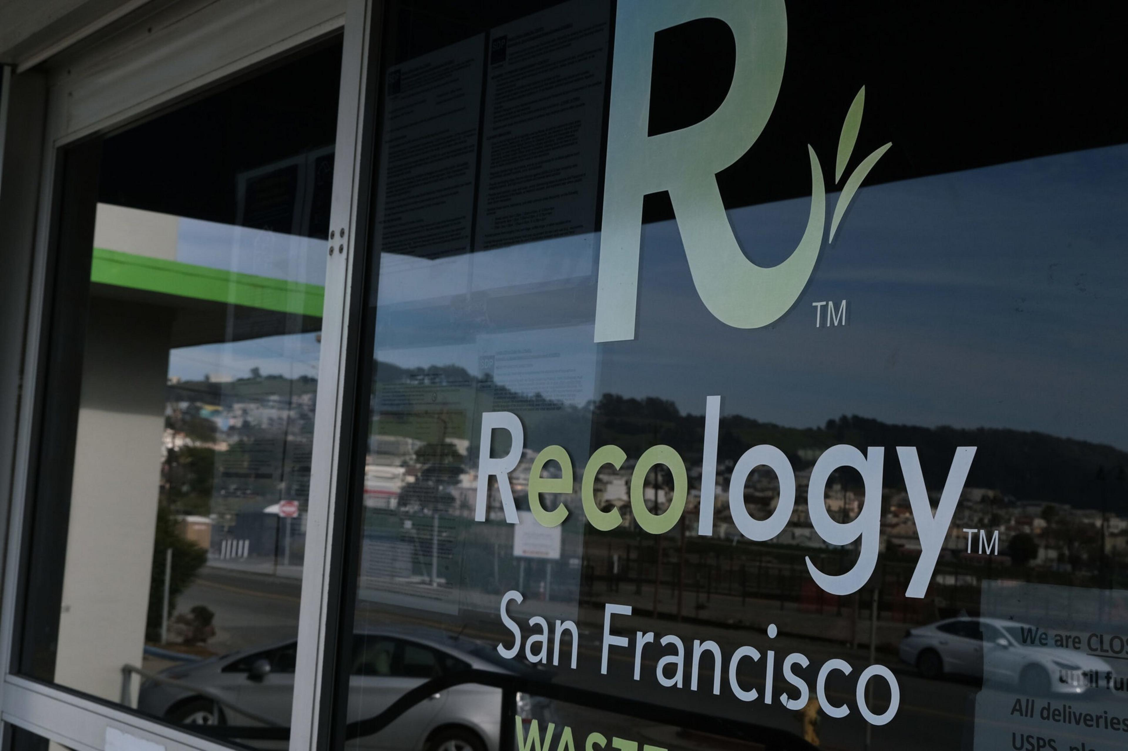 A glass door displays the "Recology San Francisco" logo with a large "R" and a leaf, reflecting cars and buildings outside.