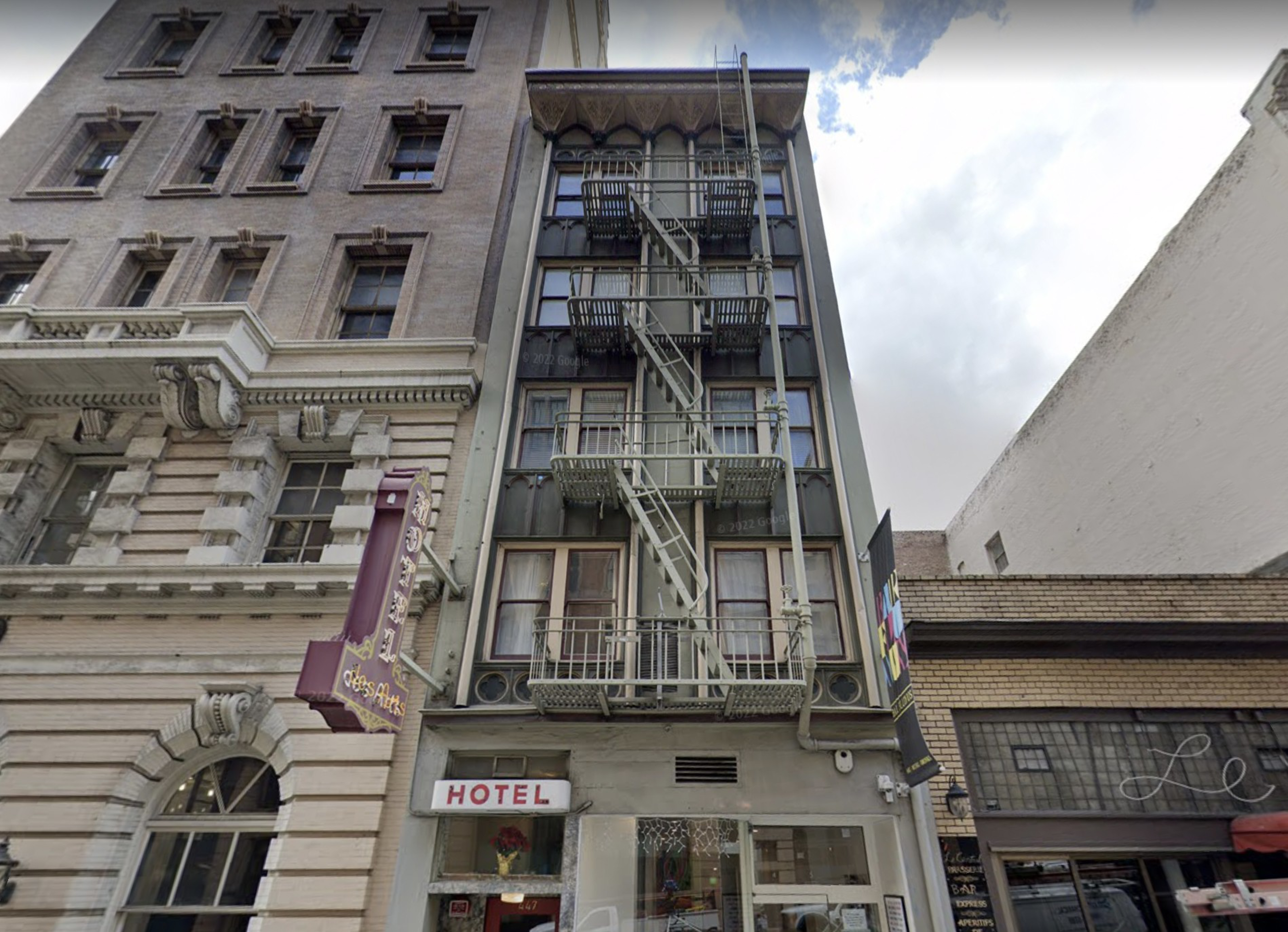 A narrow, four-story building with metal fire escapes on the front stands between two taller buildings; a small "Hotel" sign is visible above the entrance.