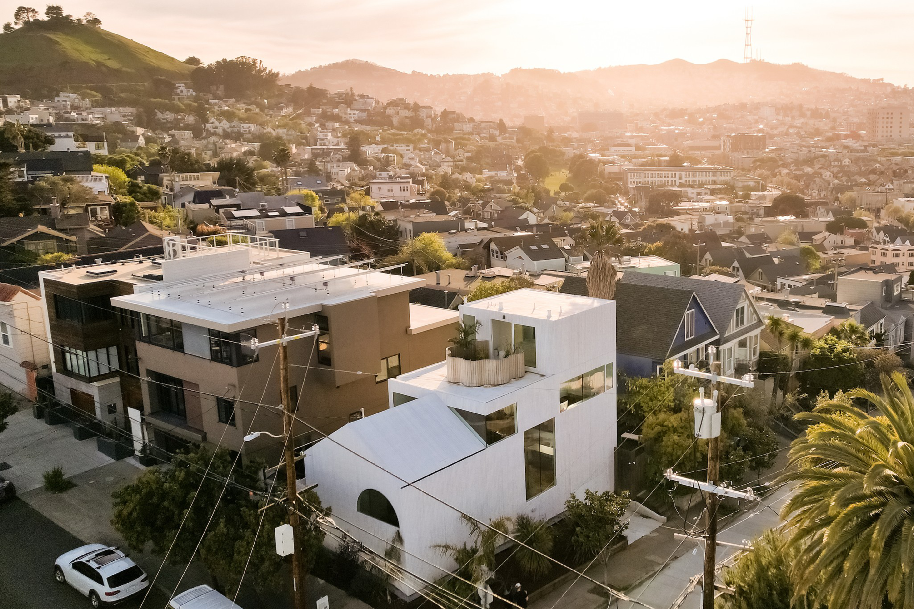 Sunset over a hilly neighborhood, spotlighting a mix of modern and traditional homes, with a distant hill and glowing sky.