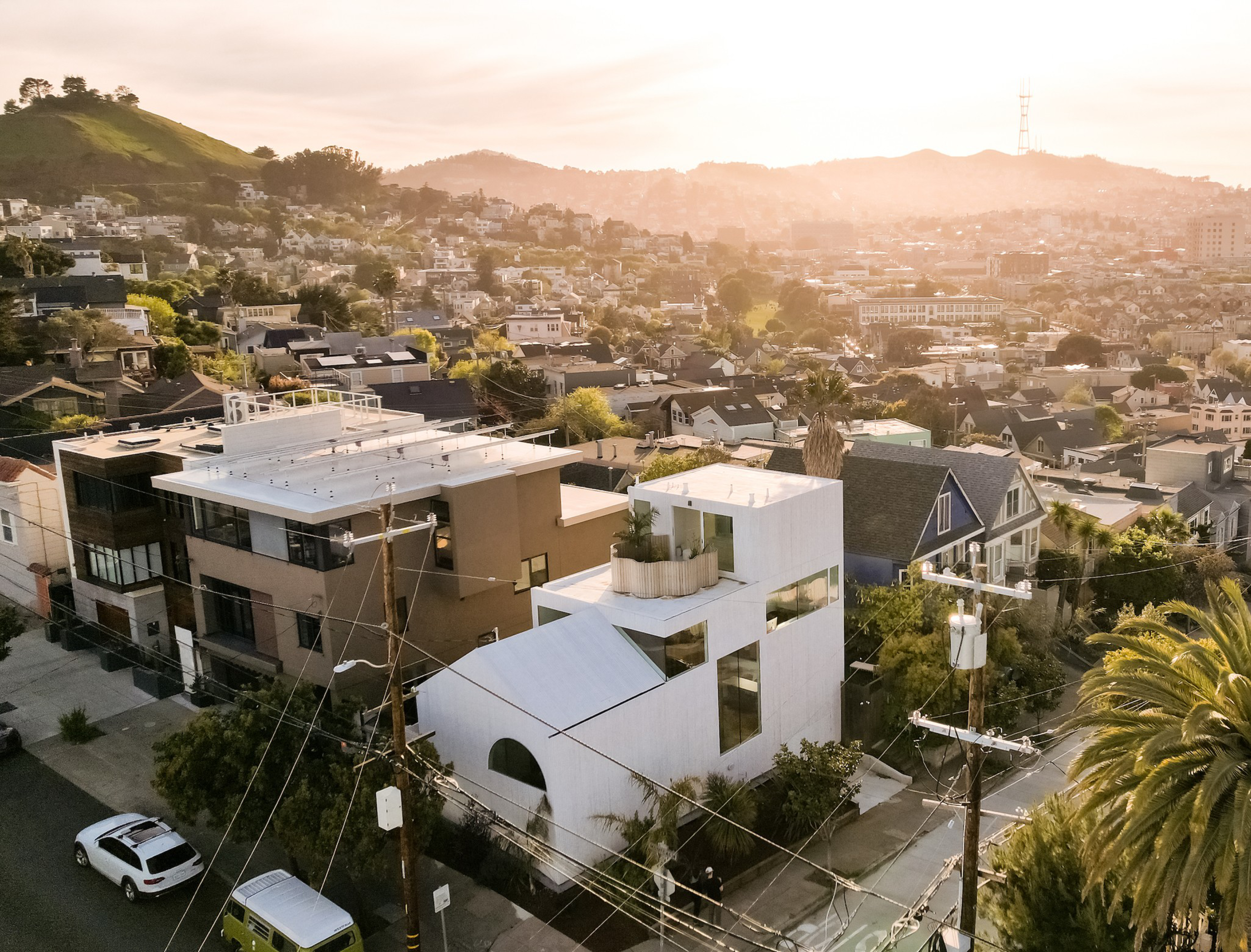 Sunset over a hilly neighborhood, spotlighting a mix of modern and traditional homes, with a distant hill and glowing sky.