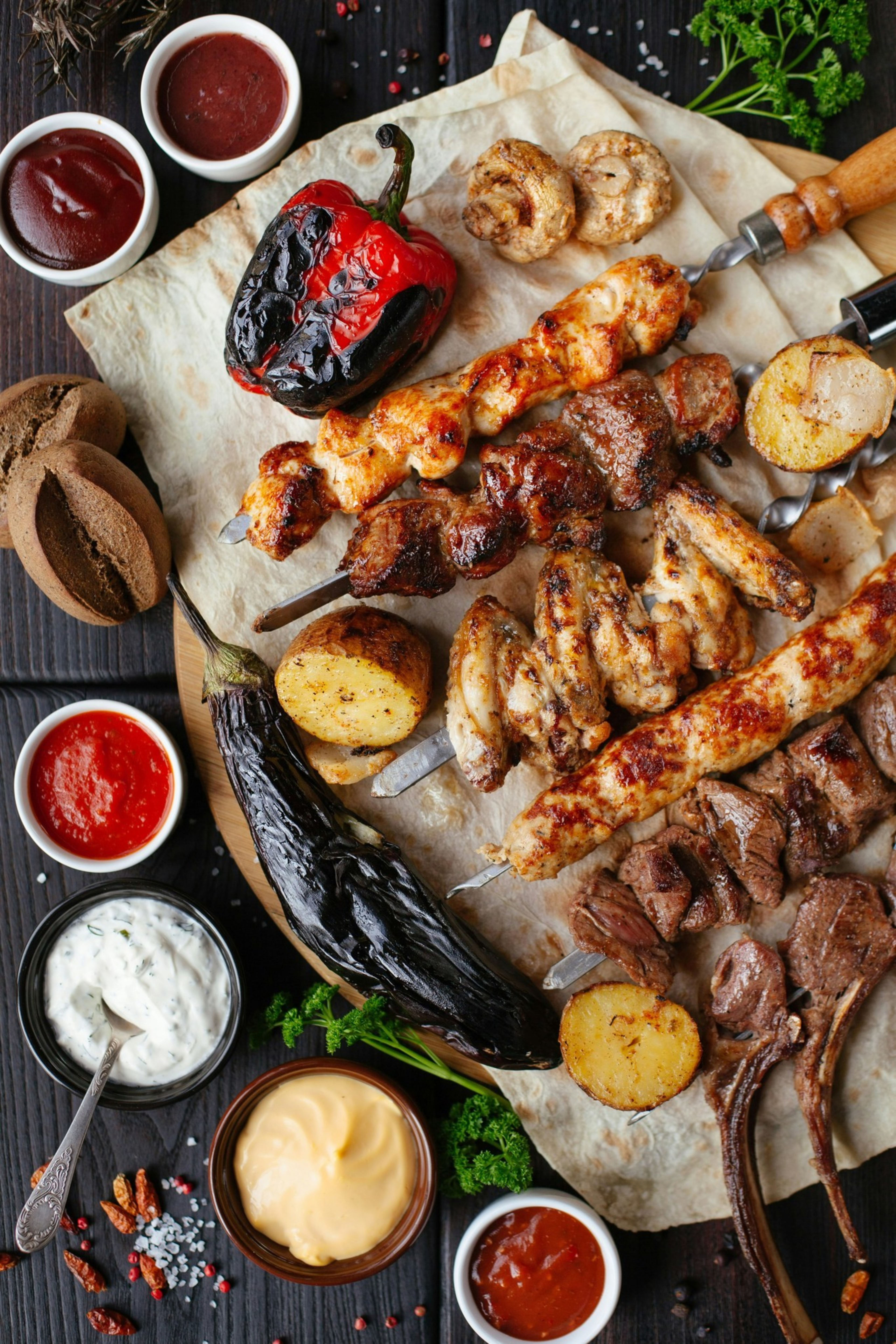 Grilled assorted skewers with chicken, beef, and vegetables including bell pepper, potatoes, eggplant, mushrooms, and various dipping sauces on flatbread.