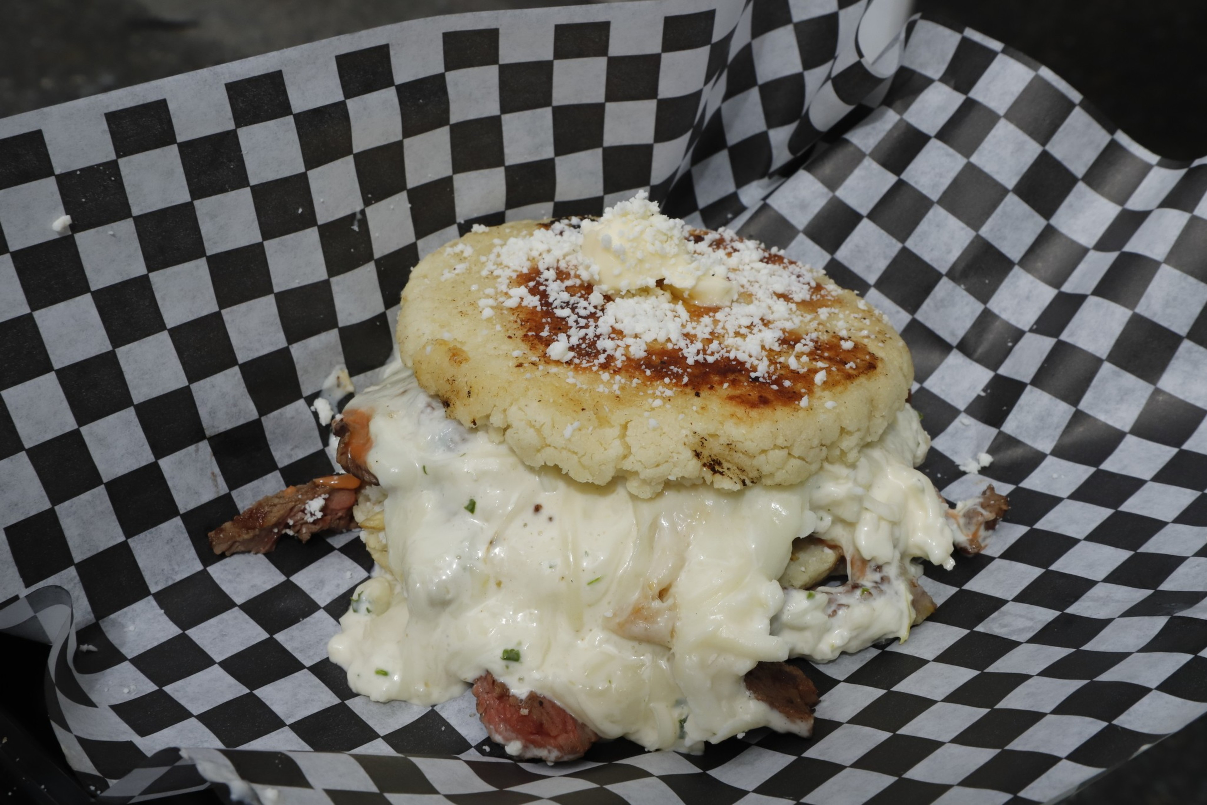 A cheesy dish with a golden-brown arepa on top, resting on black and white checkered paper.