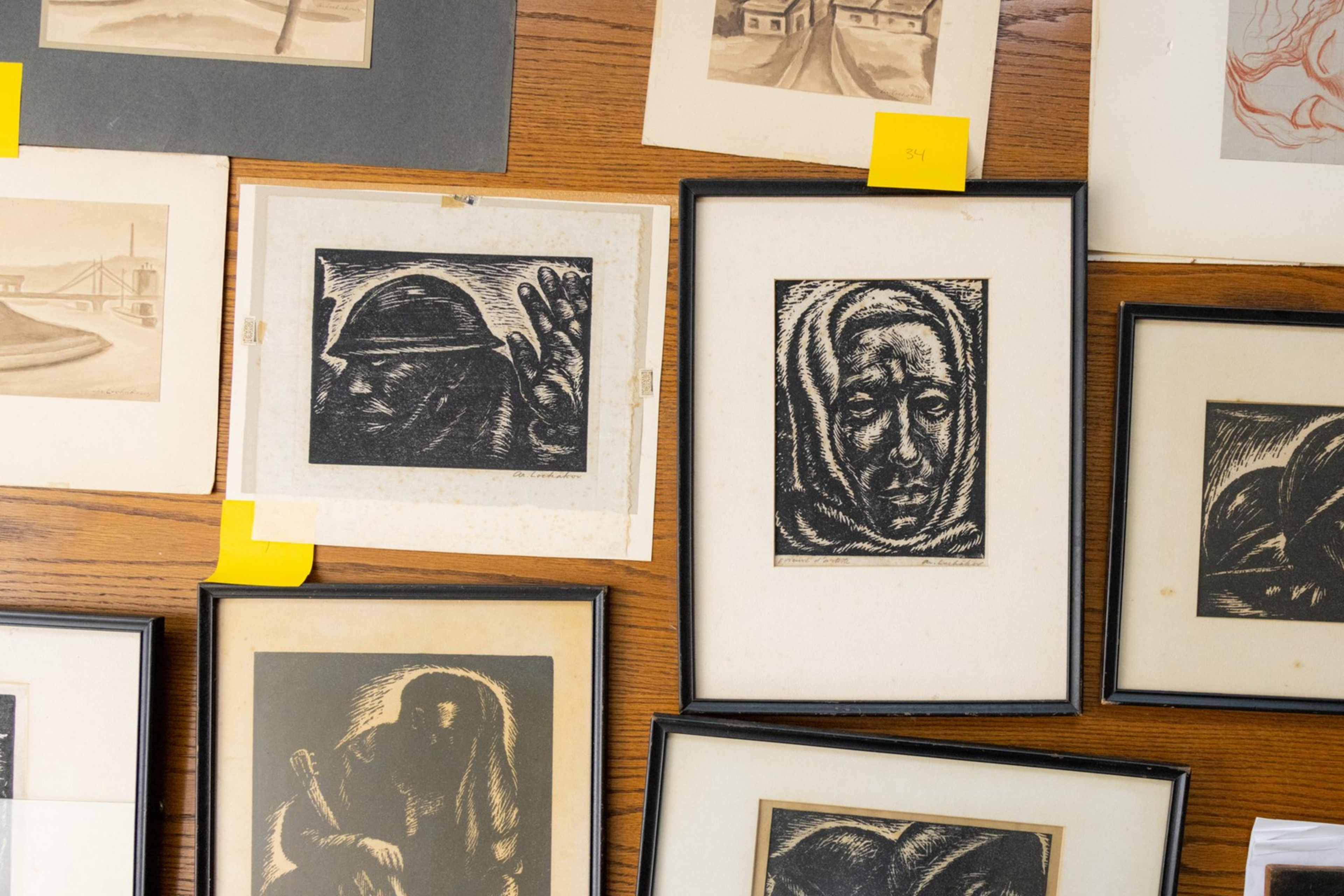 Collection of framed monochrome artworks displayed on wood, depicting various figures and abstract forms, with numbered labels.