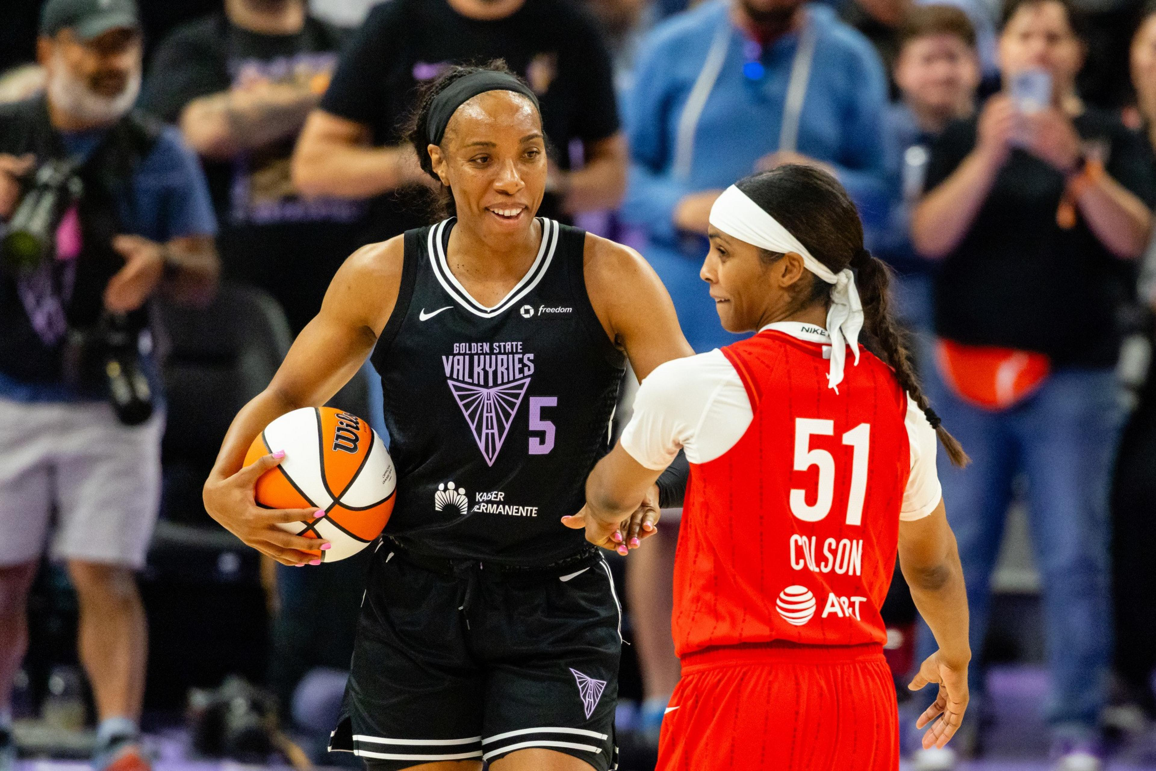Two women are playing basketball; one in a black "Golden State Valkyries" jersey with number 5 is holding the ball, and the other in a red jersey with number 51 is nearby.
