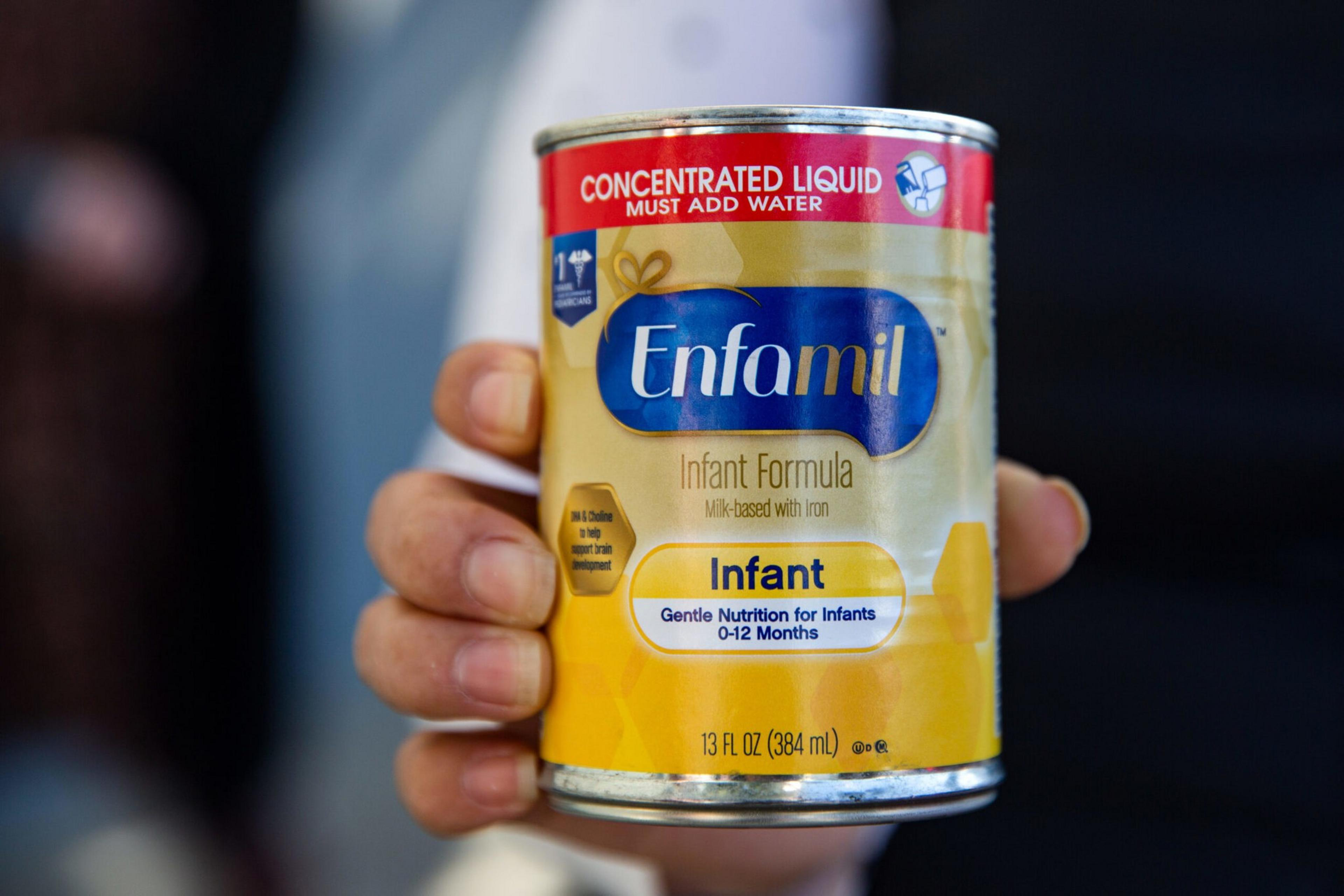 A hand holds a 13 fl oz can of Enfamil Infant Formula, labeled as concentrated liquid that must be mixed with water for infants 0-12 months.
