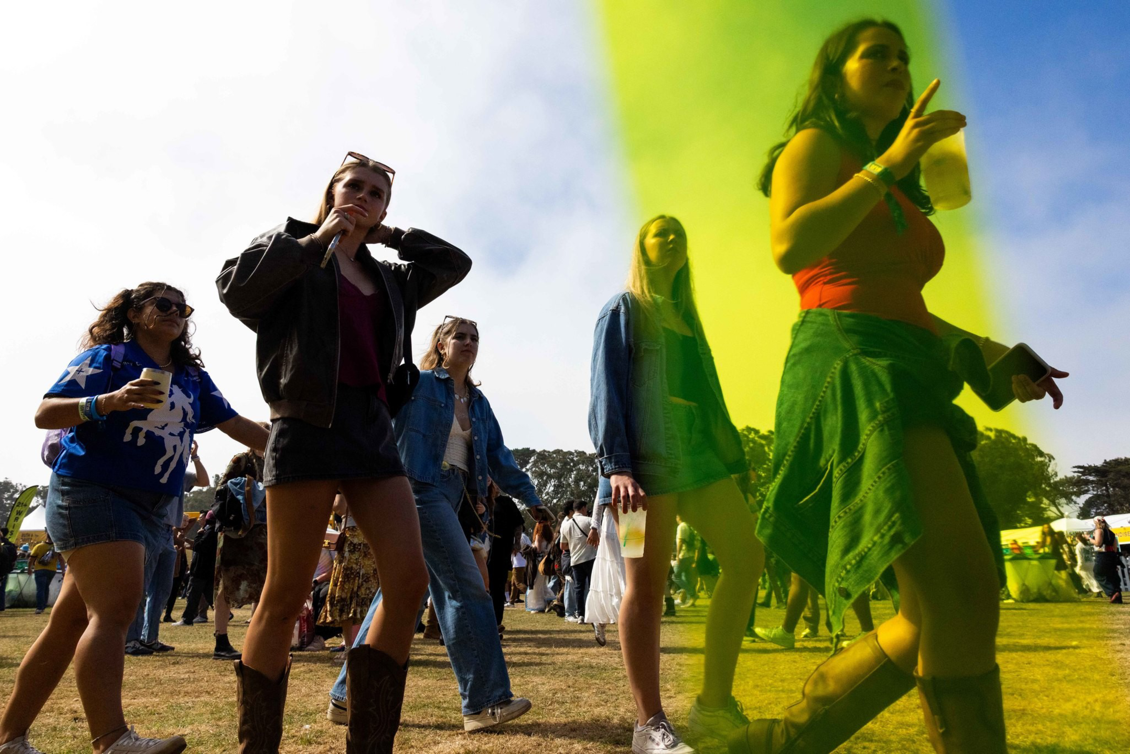 A group of young people walk on a grassy field at an outdoor event, holding drinks, with one person wearing cowboy boots and another in a denim jacket.