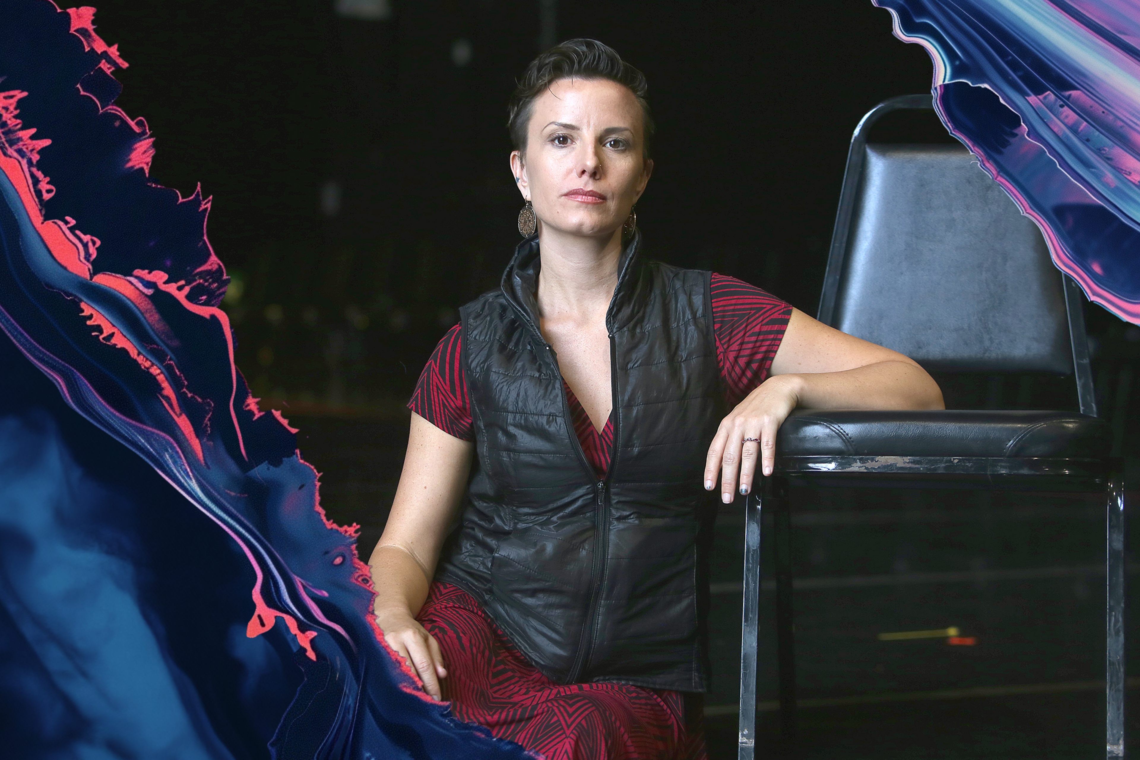 A woman in a red dress and black vest sits confidently on a chair, with abstract blue and pink swirls surrounding her.