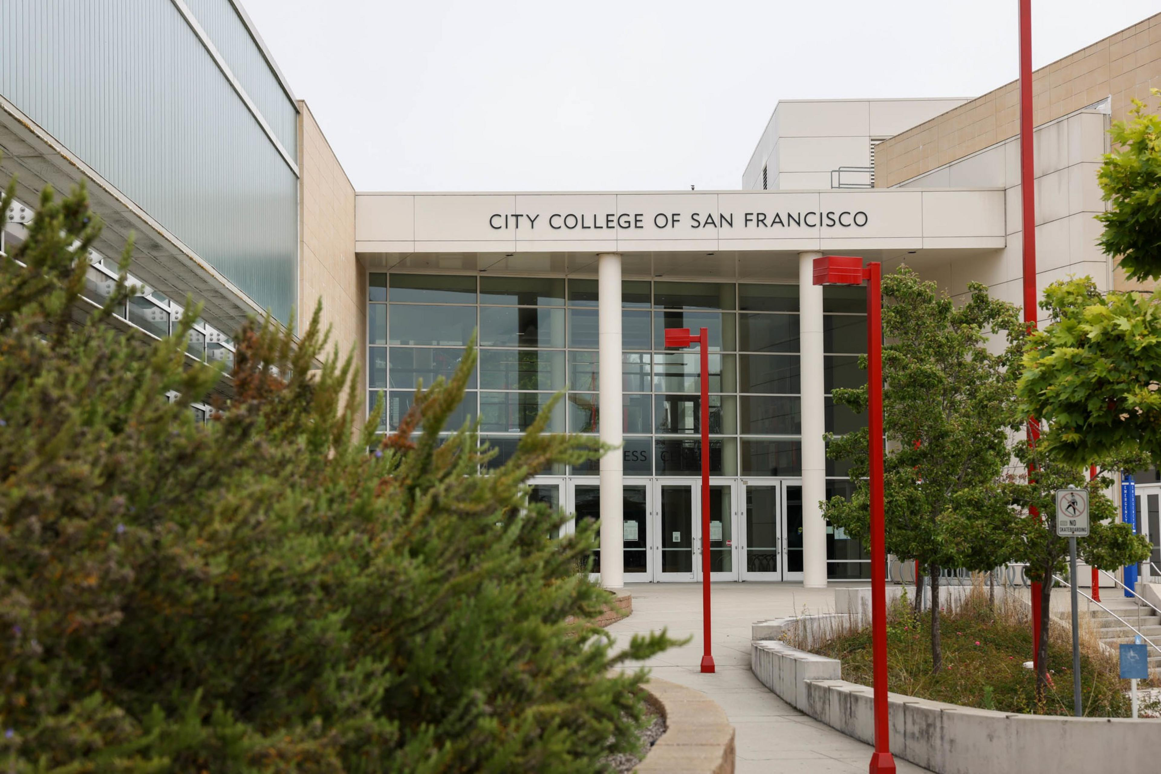 A modern college building entrance with glass doors, white pillars, red lamp posts, and greenery on both sides, labeled "City College of San Francisco."