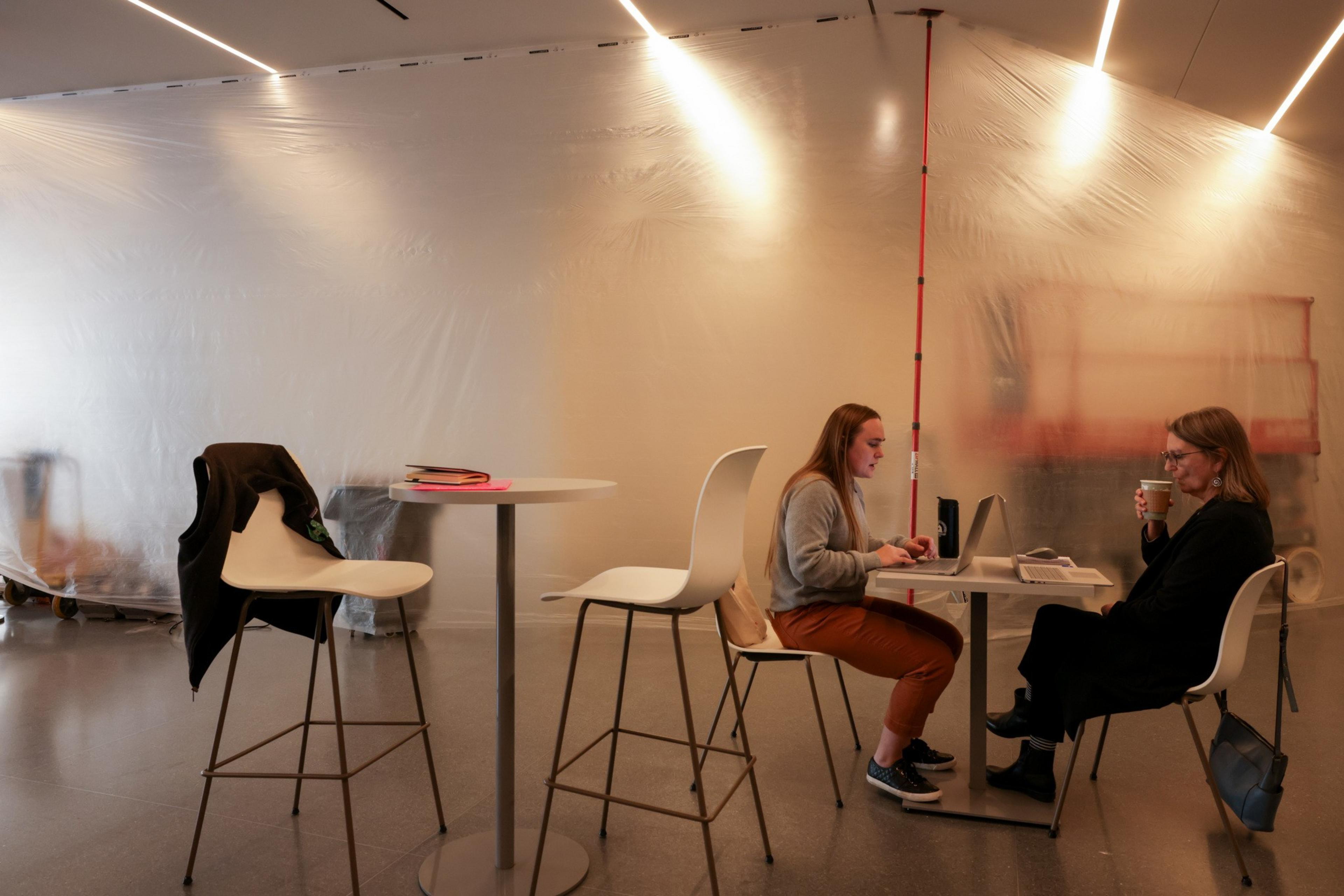 People sit at tables beside plastic sheeting. 