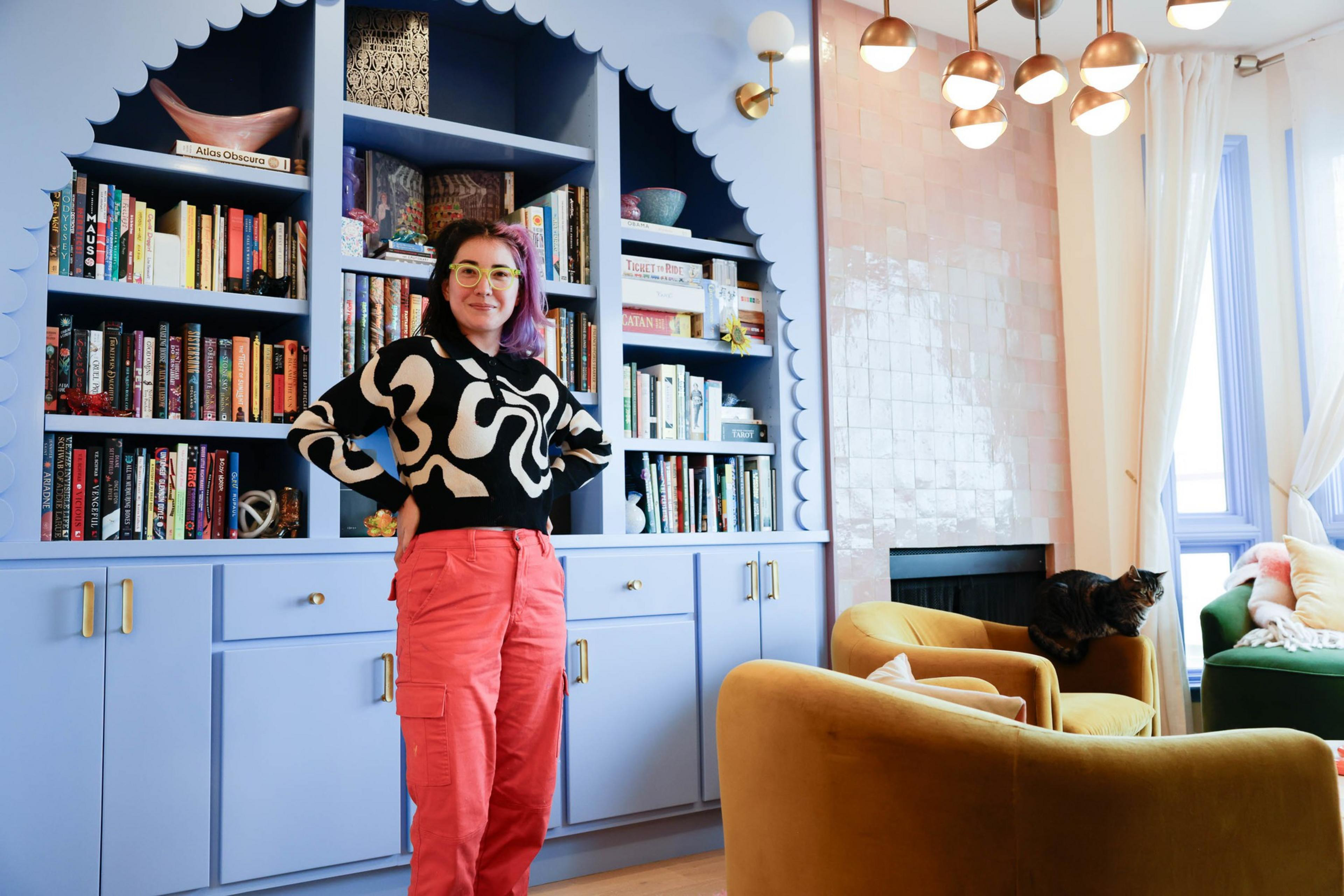 TikTok DIY design influencer Tay "BeepBoop" Nakamoto poses in front of a blue scalloped bookcase she custom designed.